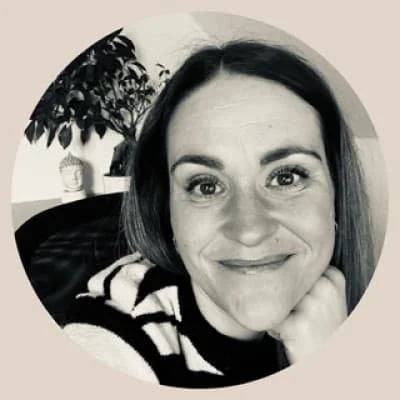 Schwarz-weiß-Porträt einer lächelnden Frau mit dunklen, schulterlangen Haaren, sitzend vor einem Pflanzen- und Deko-Hintergrund.