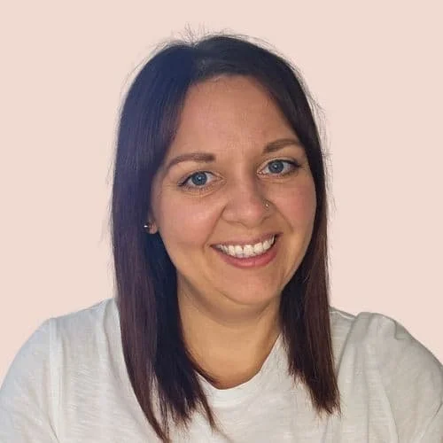 Ein Portraitfoto einer lächelnden Frau mit dunklem Haar und Nasenring vor hellem Hintergrund.