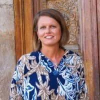 Simone in einer gemusterten Bluse vor einer Holztuer