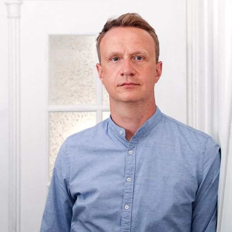 Ein Mann in einem blauen Hemd steht vor einer weißen Tür mit Fenster