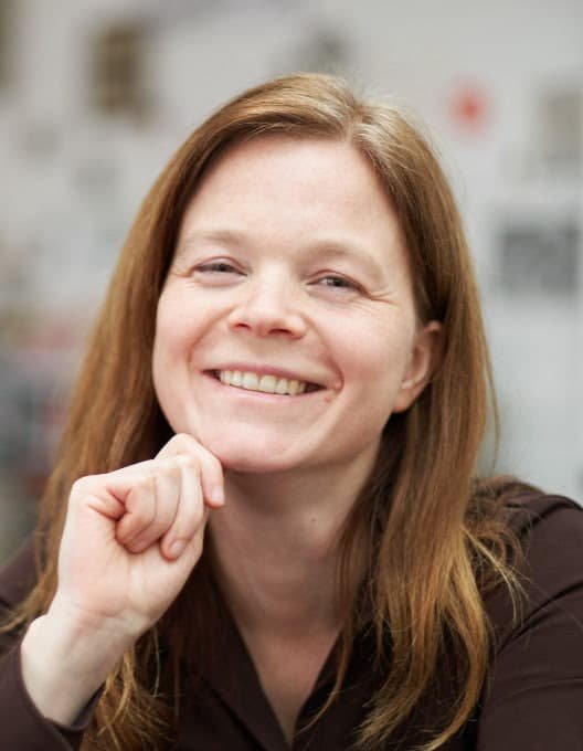 Jana hat braunes langes Haar und laechelt in die Kamera