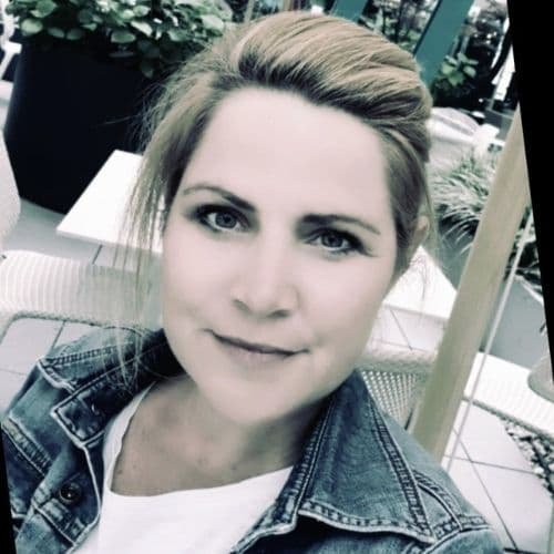 Nahaufnahme eines lächelnden jungen Frau mit kurzen braunen Haaren, trägt eine Jeansjacke und sitzt im Freien.