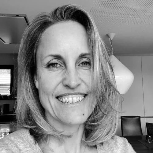 Schwarz-weiß-Foto einer lächelnden Frau mit Schulterlänge Haaren in einem modernen Raum.