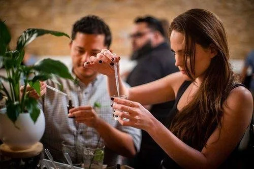 A woman pours a drink into a glass at a social gathering with other people in the background.