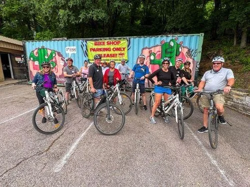 Group of nine people with bicycles standing in front of a colorful wall and a yellow sign that says 'Bike Shop Parking Only, Please'.