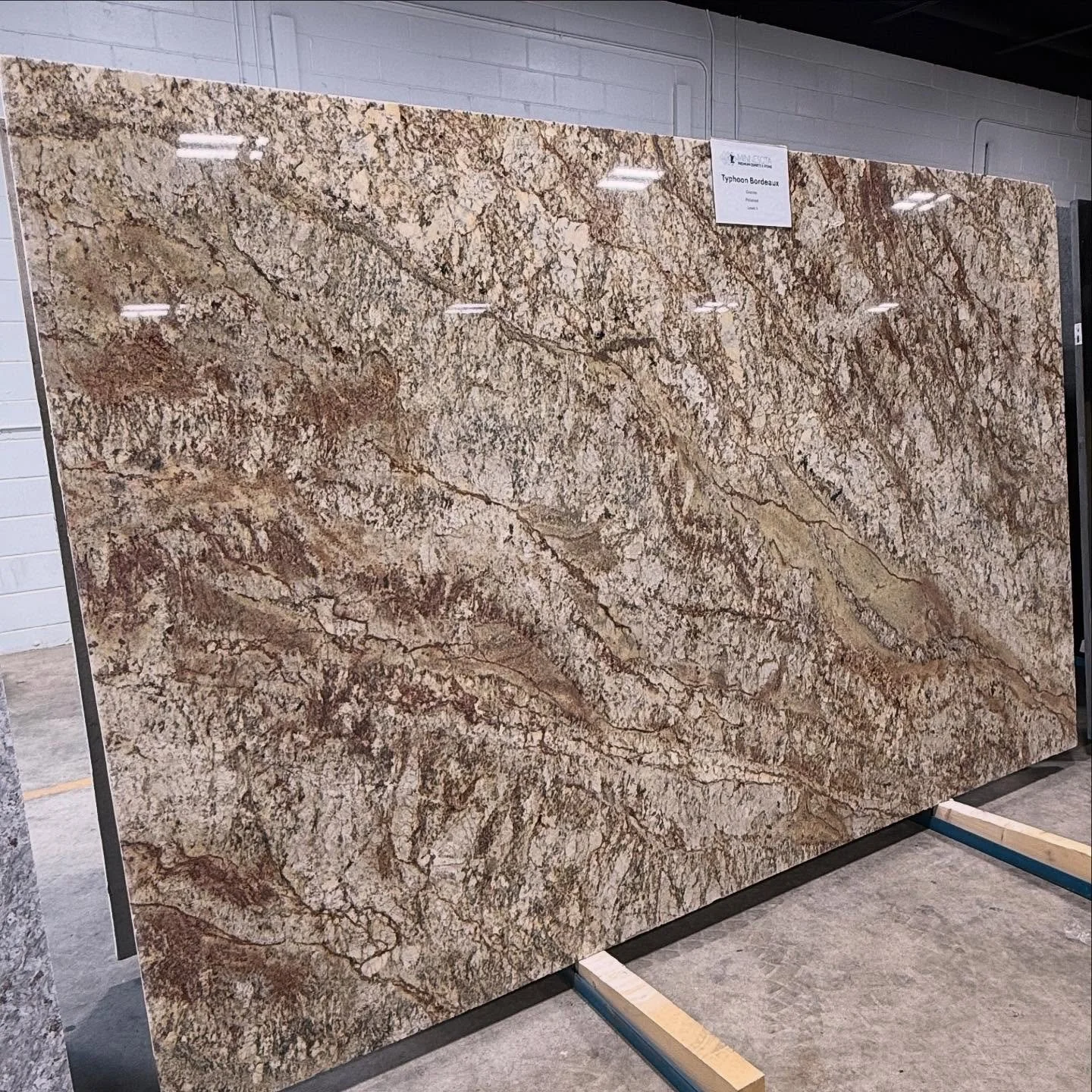 New Arrival! Typhoon Bordeaux Granite! This stunning granite offers a rich blend of gold, cream, burgundy, and gray veining that swirls across the surface like a natural masterpiece. Perfect for clients looking to make a statement with warmth, depth,