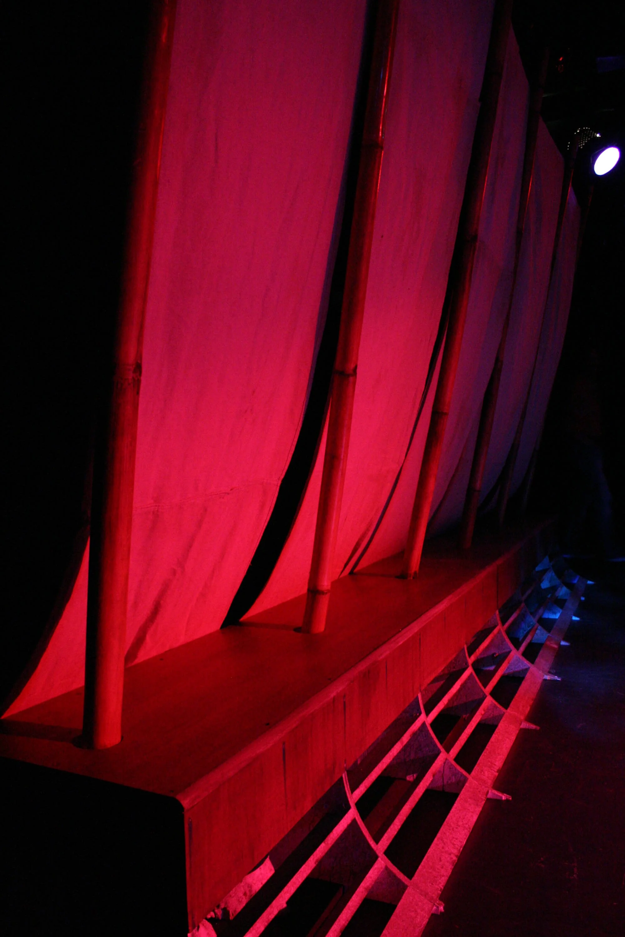 Colorful indoor stage with red and purple lighting, bamboo poles, and a curved structure at the front.