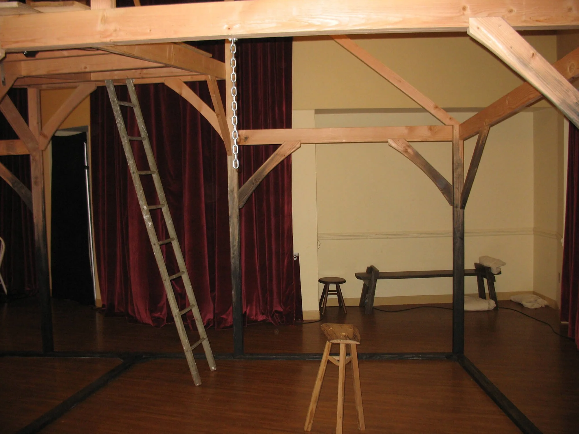 Interior of a room with a wooden loft structure, ladder, stools, and red curtains.