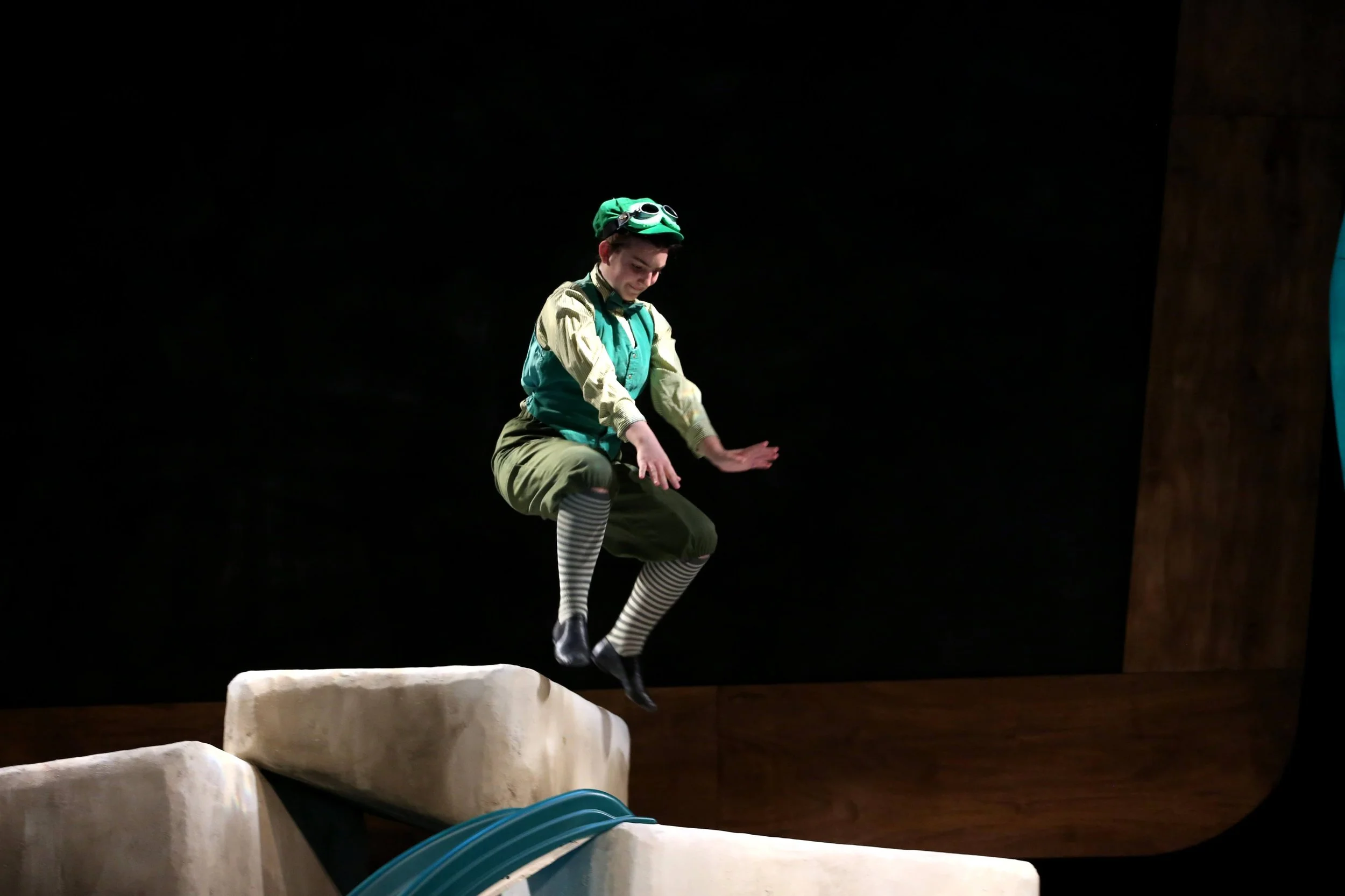 A person dressed as a jester or clown is jumping off a stone platform during a theatrical performance.