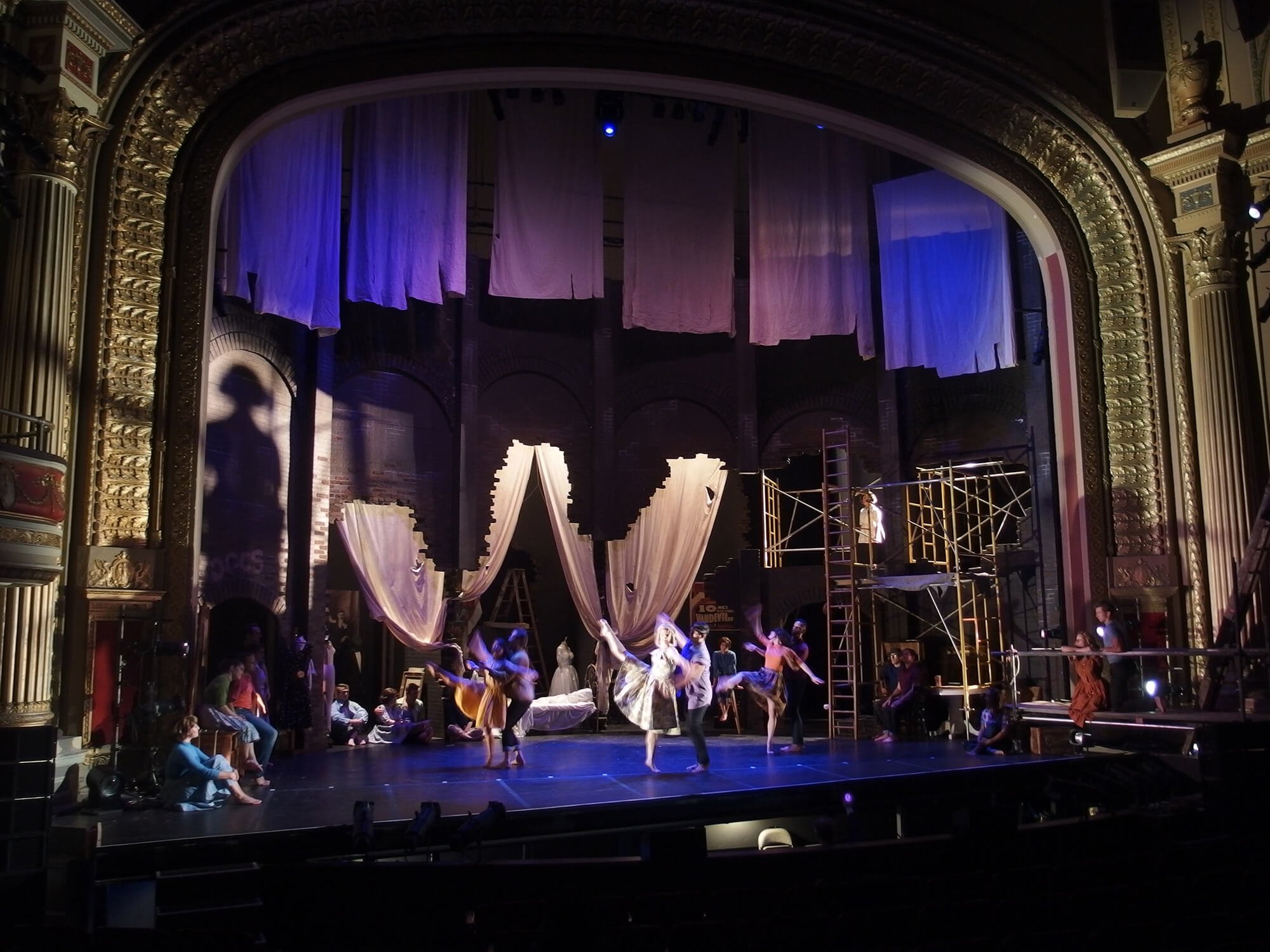 Stage with theatrical set, dancers performing, and scaffolding on right side in a theater.