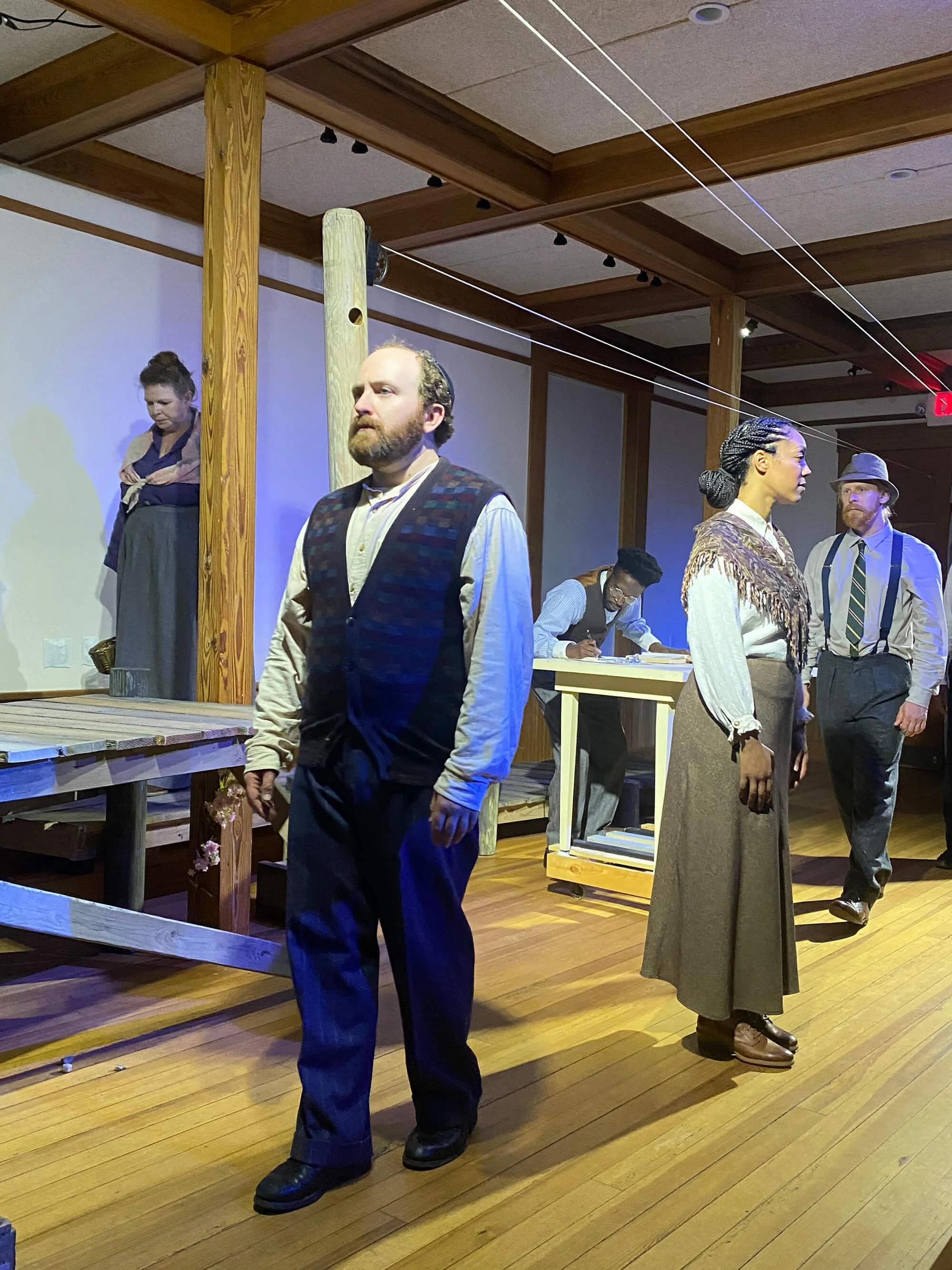 Life-sized wax figures of five individuals in period clothing from the early 20th century, arranged in a scene resembling a rural or small-town setting with wooden floors and beams.