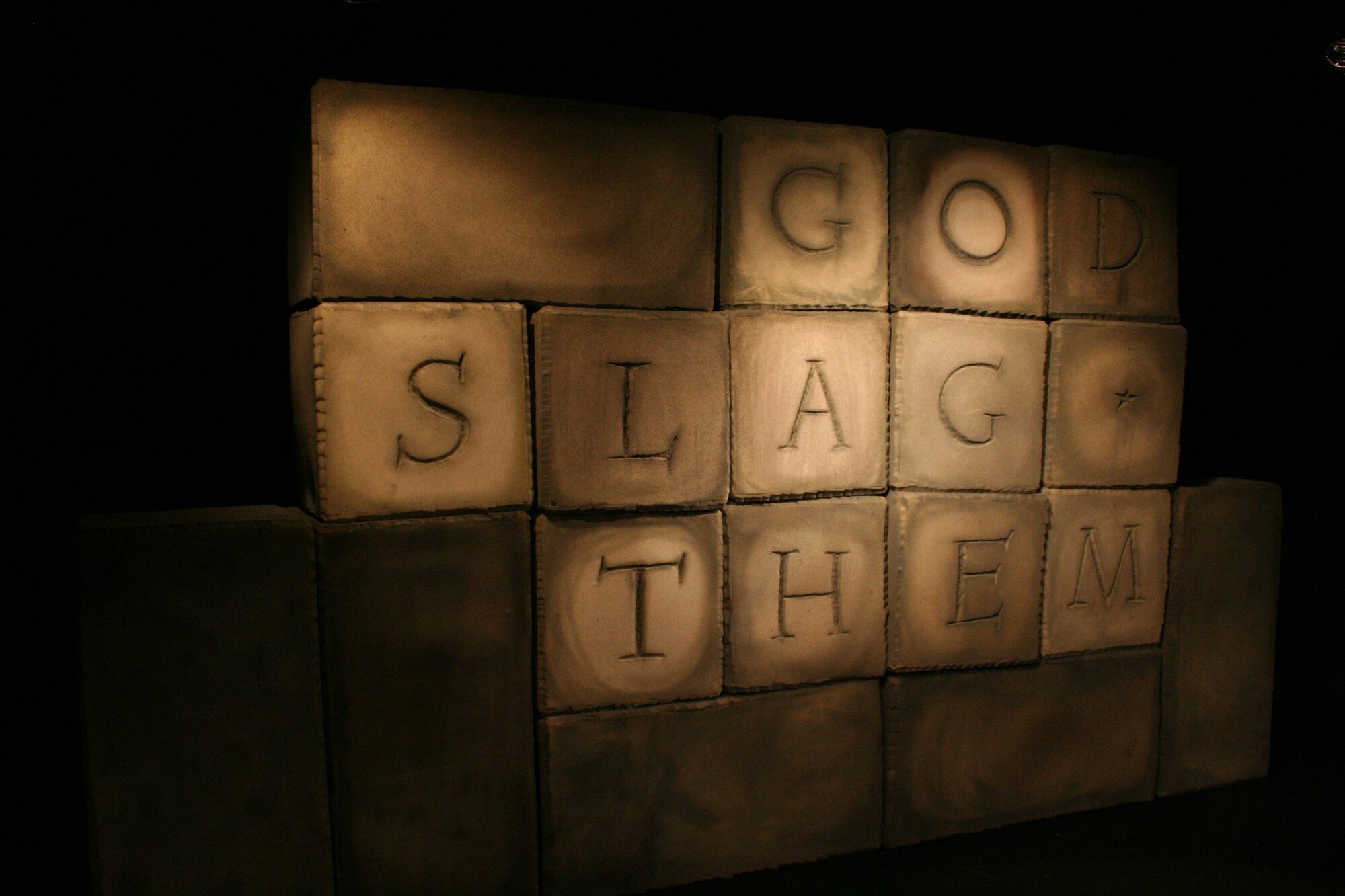 Stacked beige bricks spelling out 'God Slay the M' with the phrase arranged in three rows.