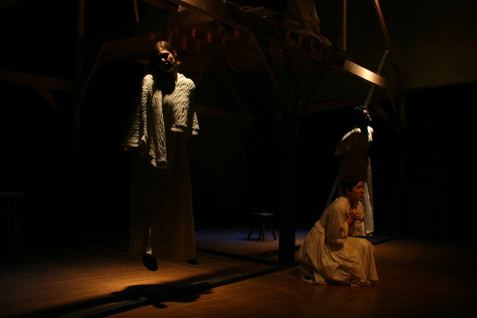 Three women in period costumes performing on stage with dark background and wooden scaffolding.