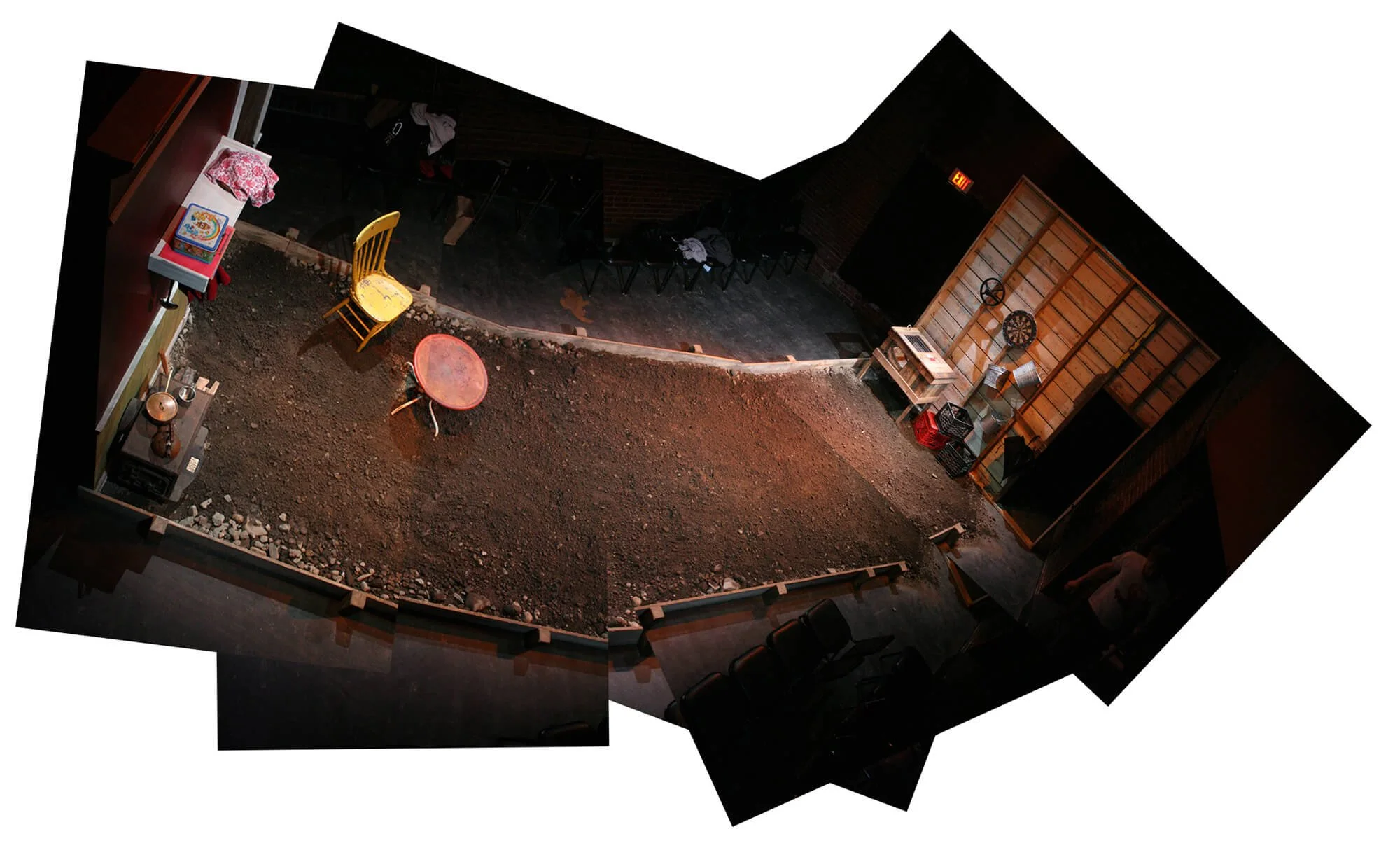 Indoor space with a dirt floor, surrounded by chairs and various items, resembling a stage or set area for a performance or event.