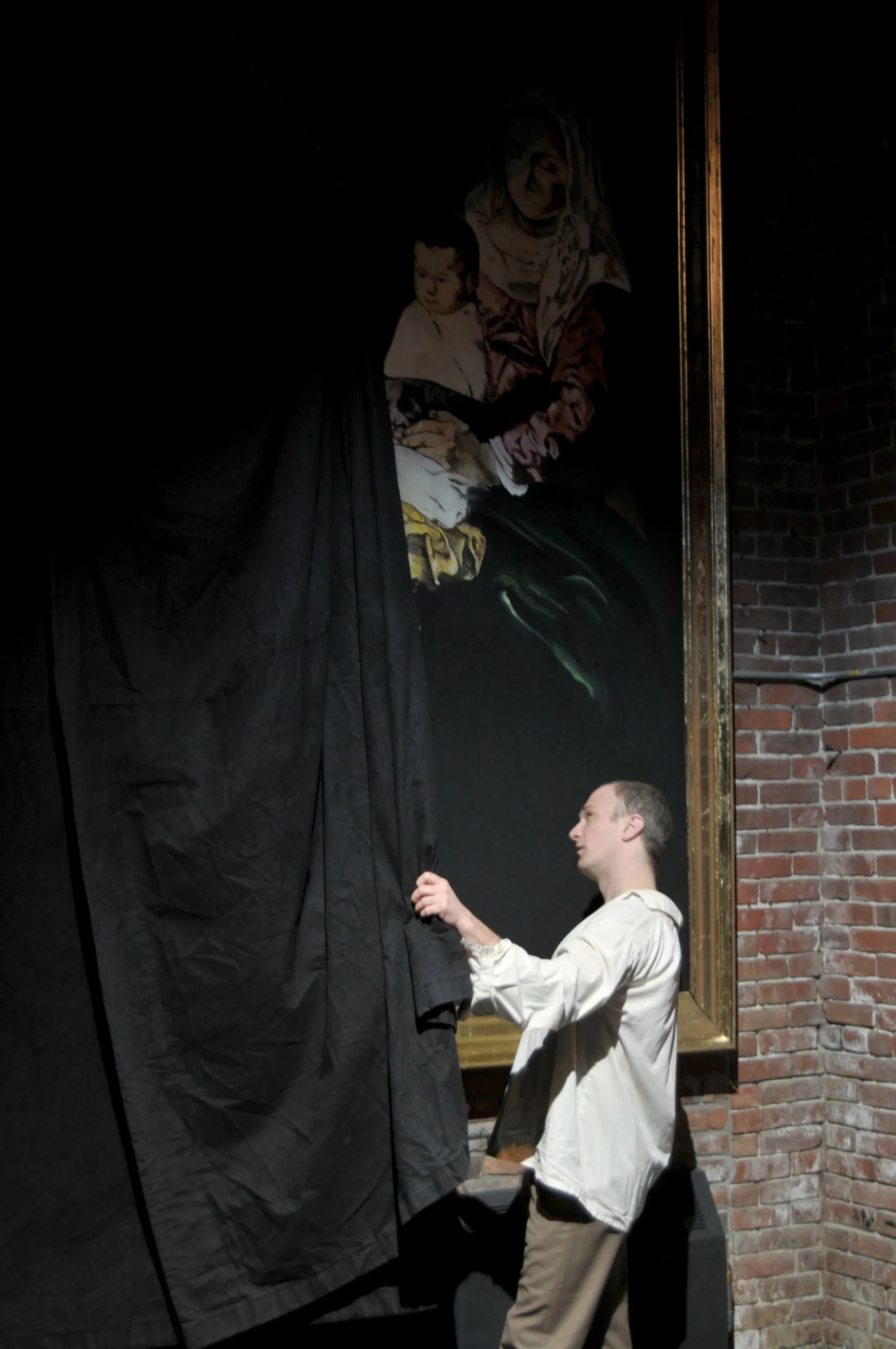 A man unveiling a painting in an art gallery with exposed brick wall.