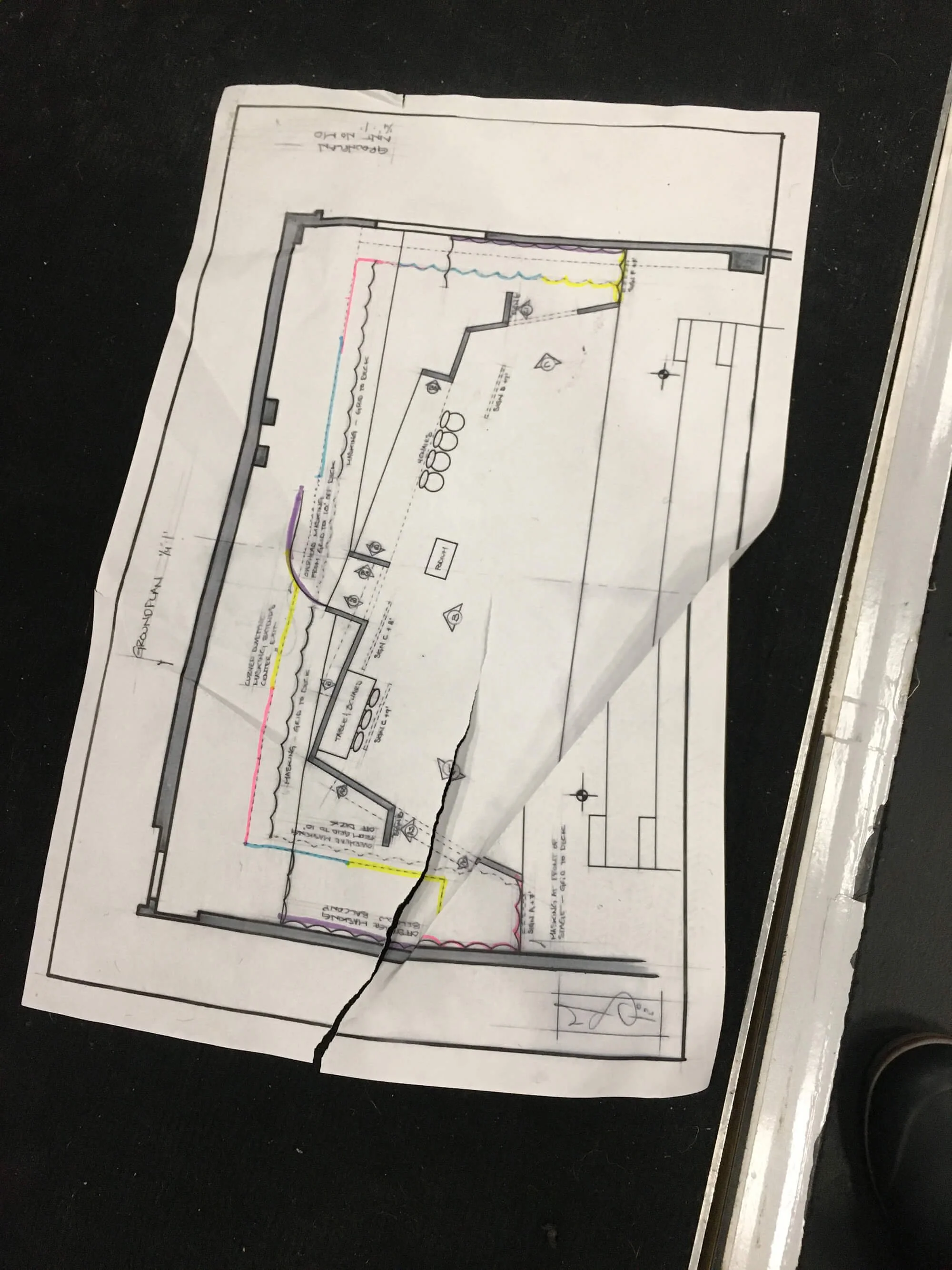 A folded architectural blueprint on black surface showing a building layout with exterior walls, interior rooms, and annotations.