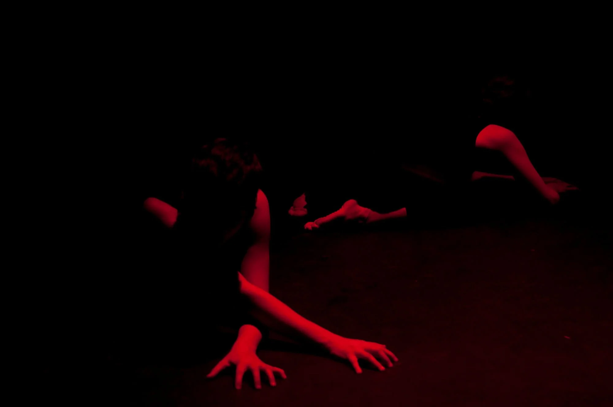 Three dancers on a dark stage with red lighting, performing in a contemporary dance pose.