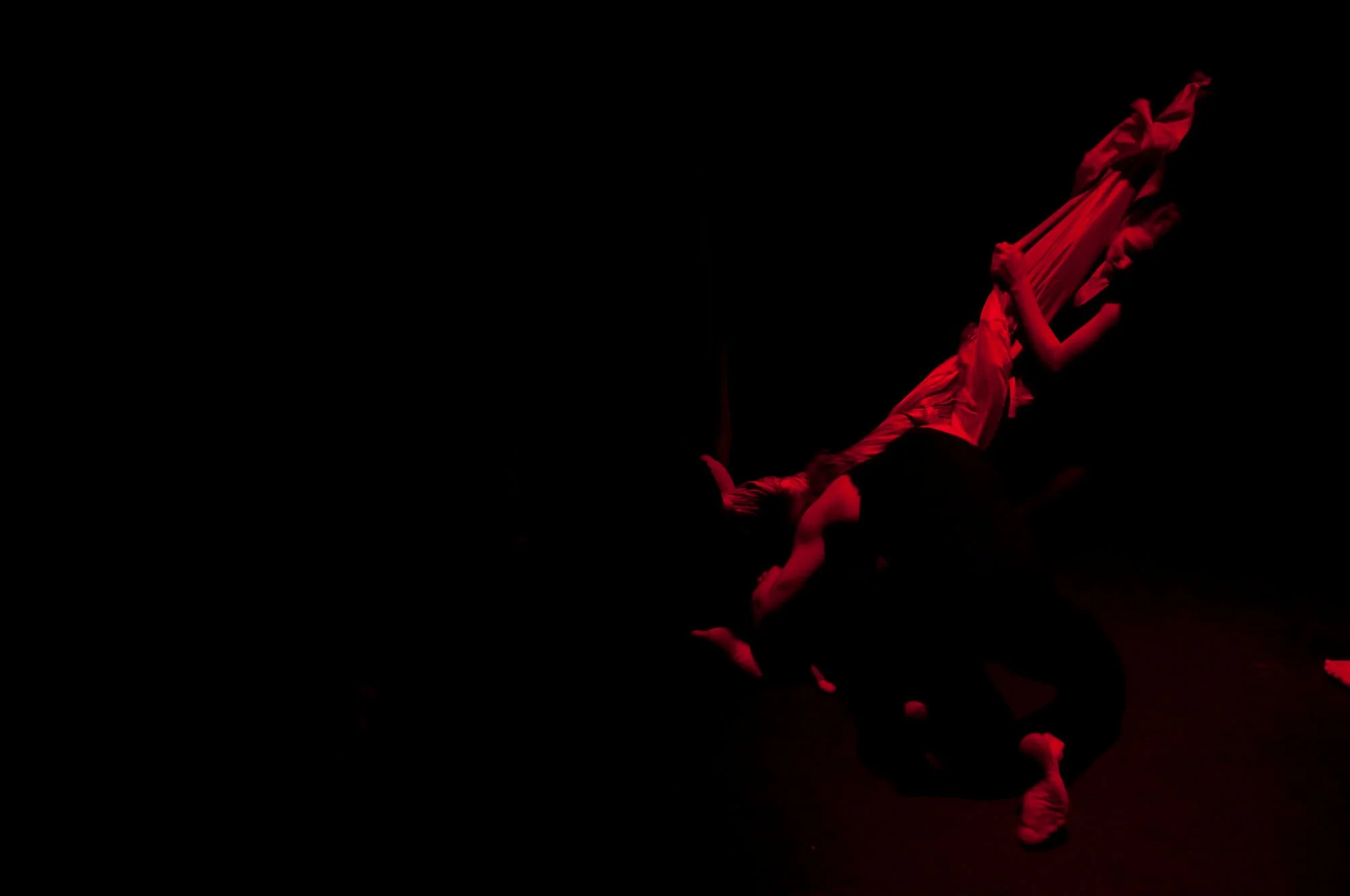 A person on stage performing an acrobatic act, illuminated by red lighting, with their body upside down and supported by another performer.