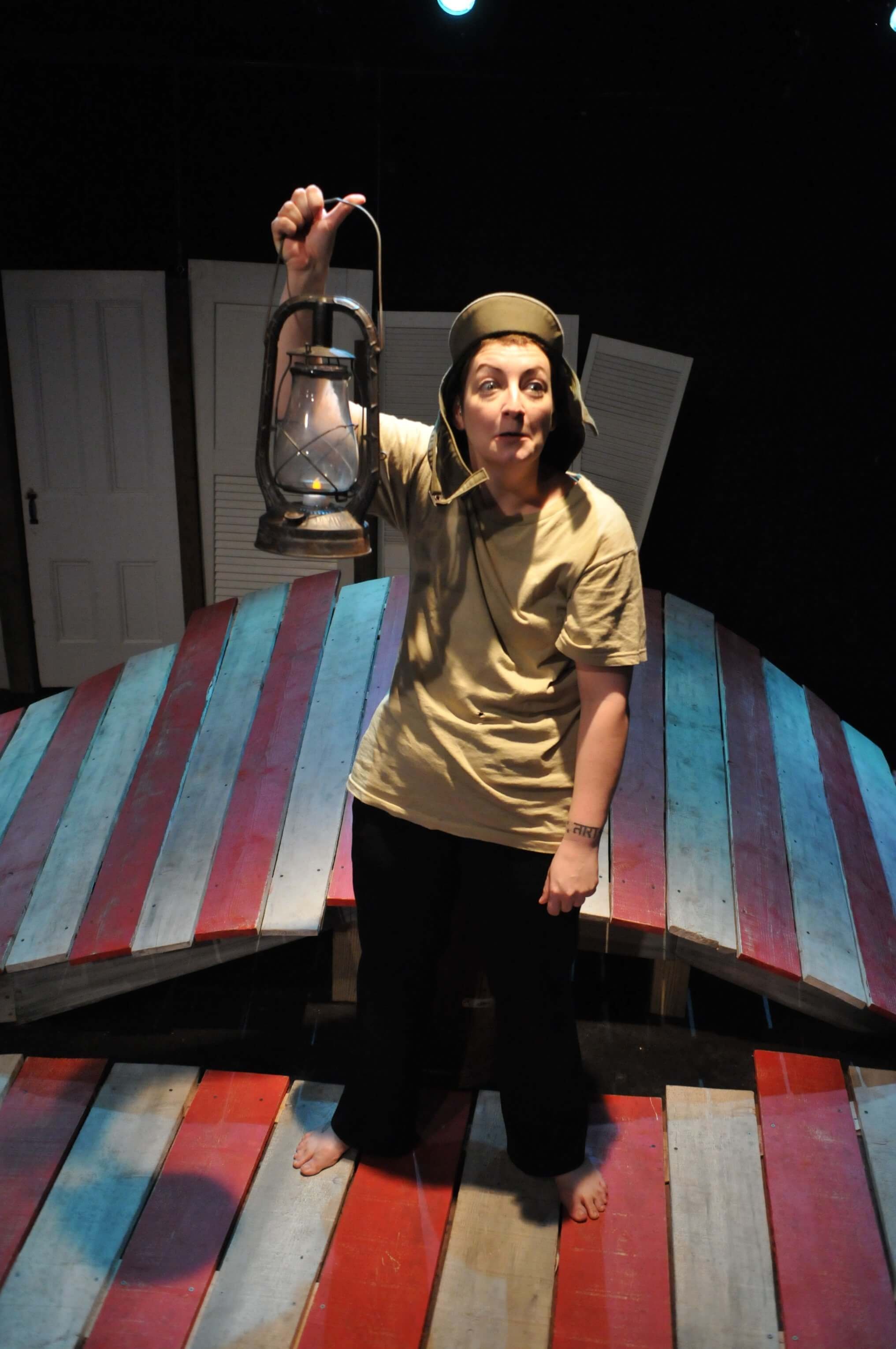 Woman holding lantern on colorful wooden stage in indoor setting.