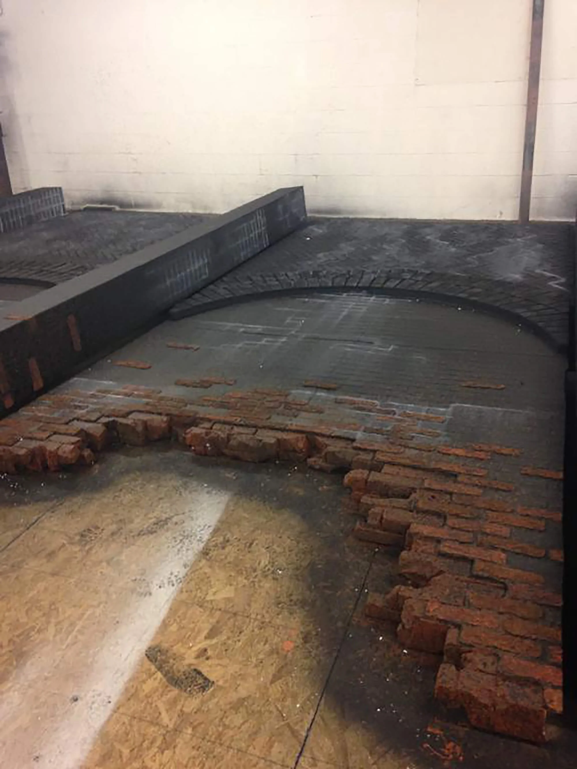 Interior of an industrial space under renovation, showing exposed brick wall, construction materials, and a partially finished floor.
