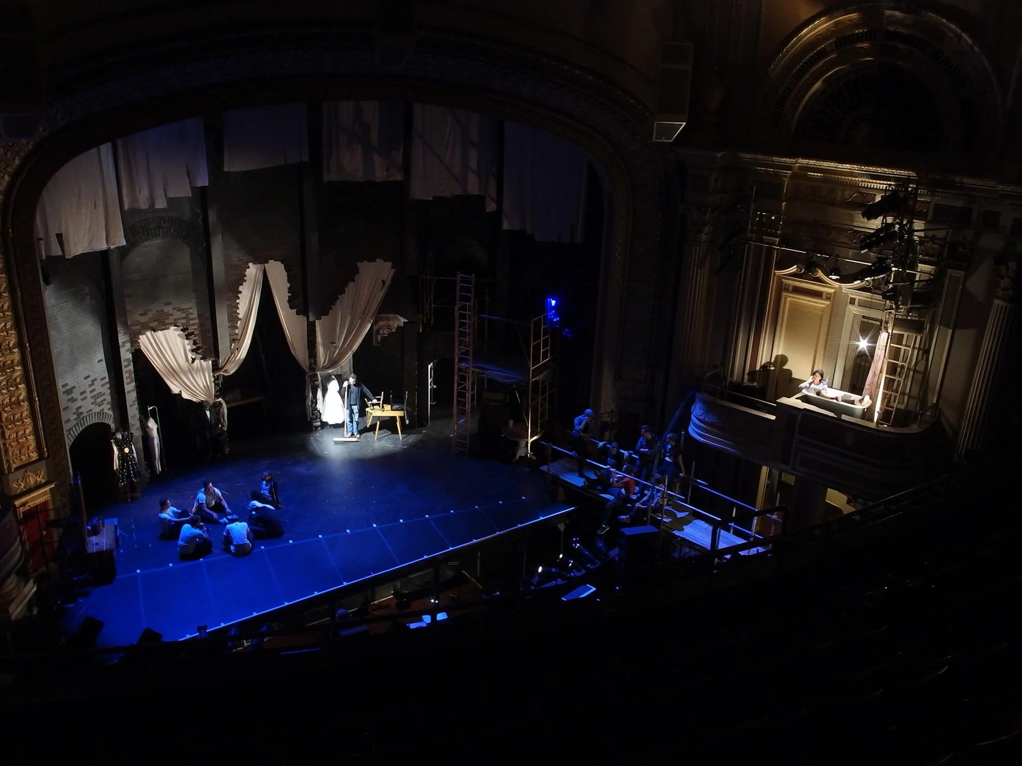 Theater stage set for a performance with curtains, lighting, and people preparing behind the scenes.