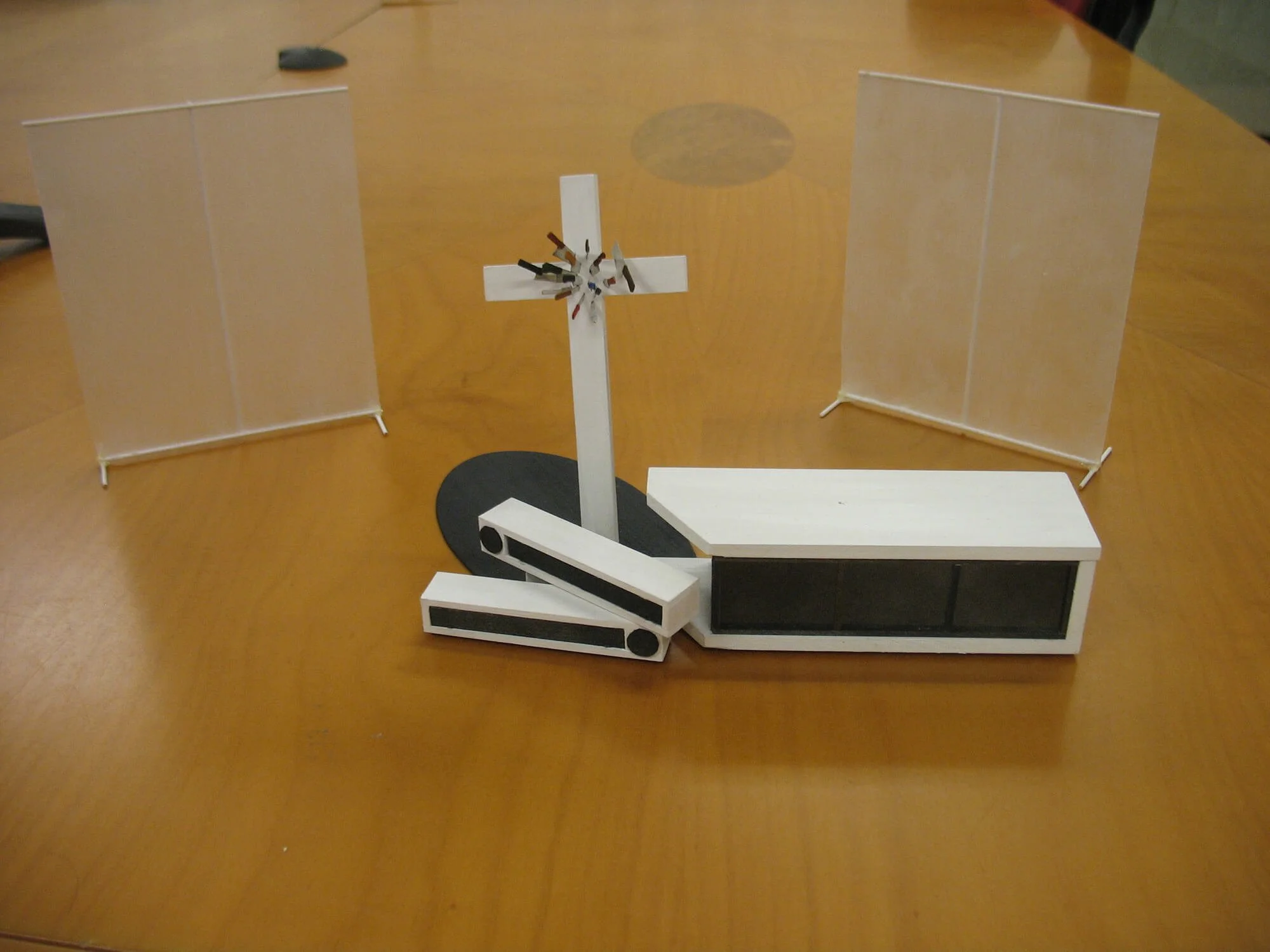 A small wooden functioning model of a steam engine on a wooden table, with two transparent dividers behind it.