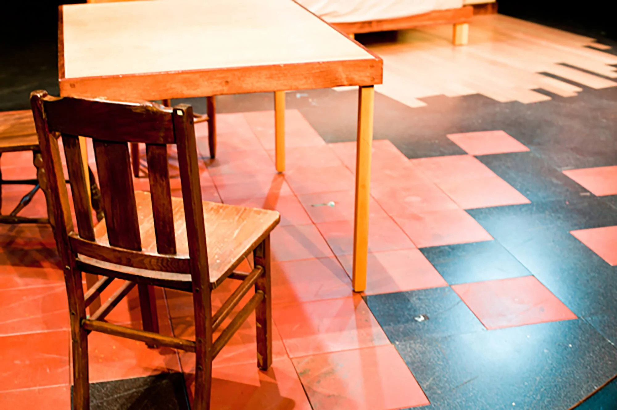 Empty wooden chair and table in a room with red and black tile flooring.