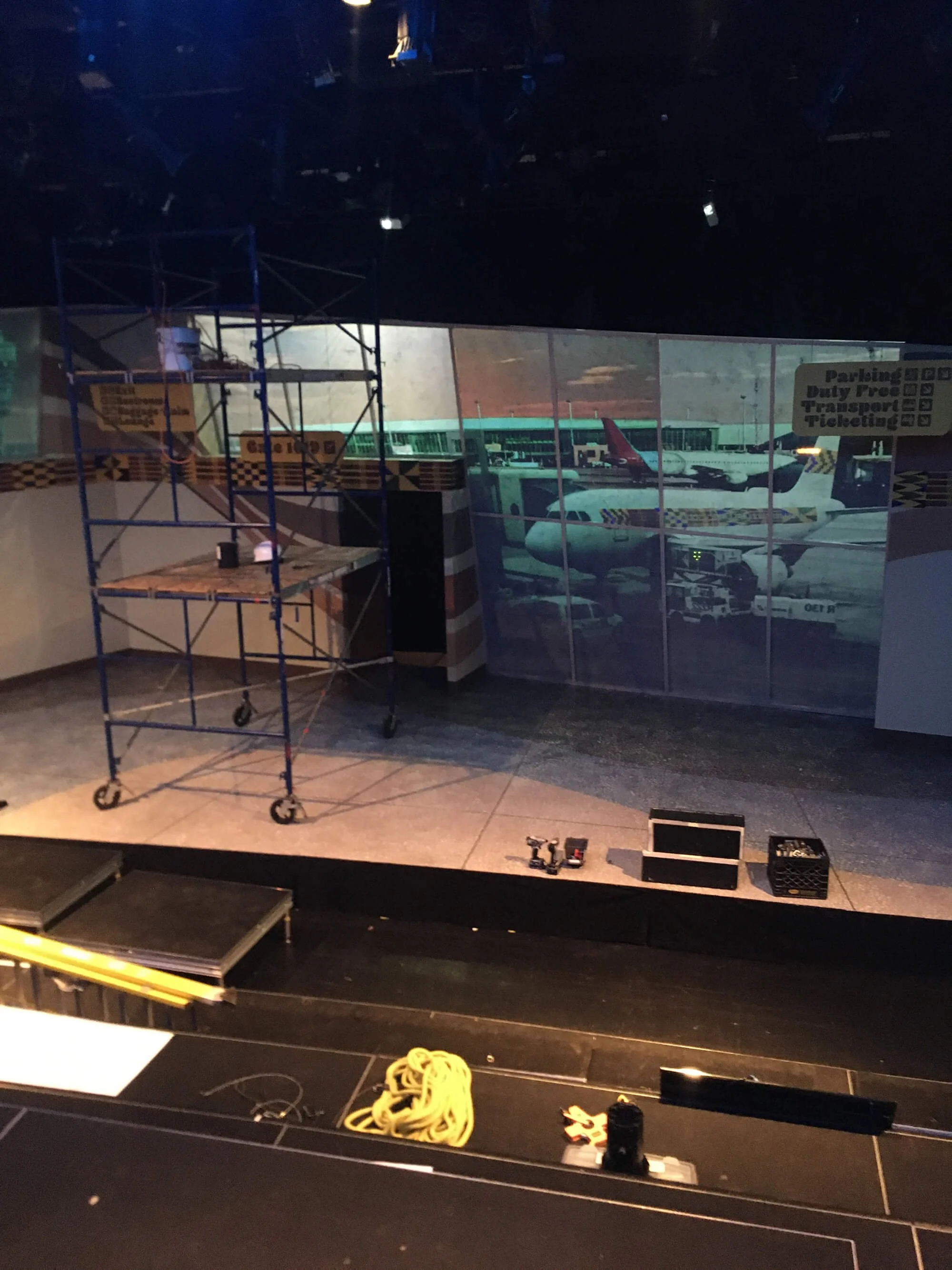 Empty stage with scaffolding, tools, and a background projection of an airport with airplanes and airport vehicles.
