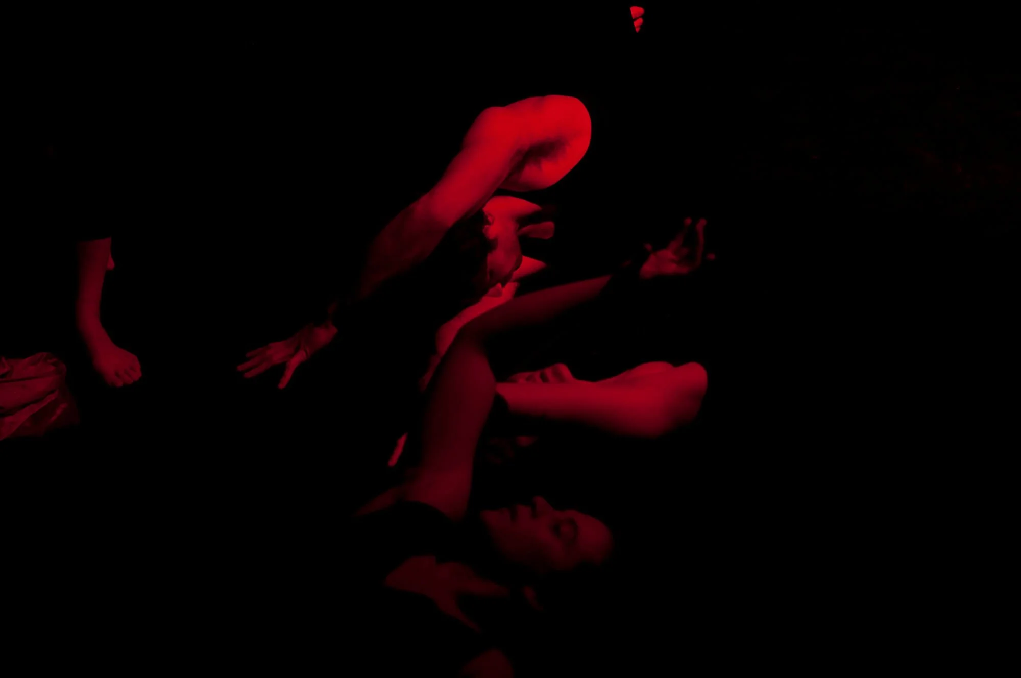 Two people are performing a contortion act on stage, illuminated by red lighting, with one person arching their back and the other supporting.
