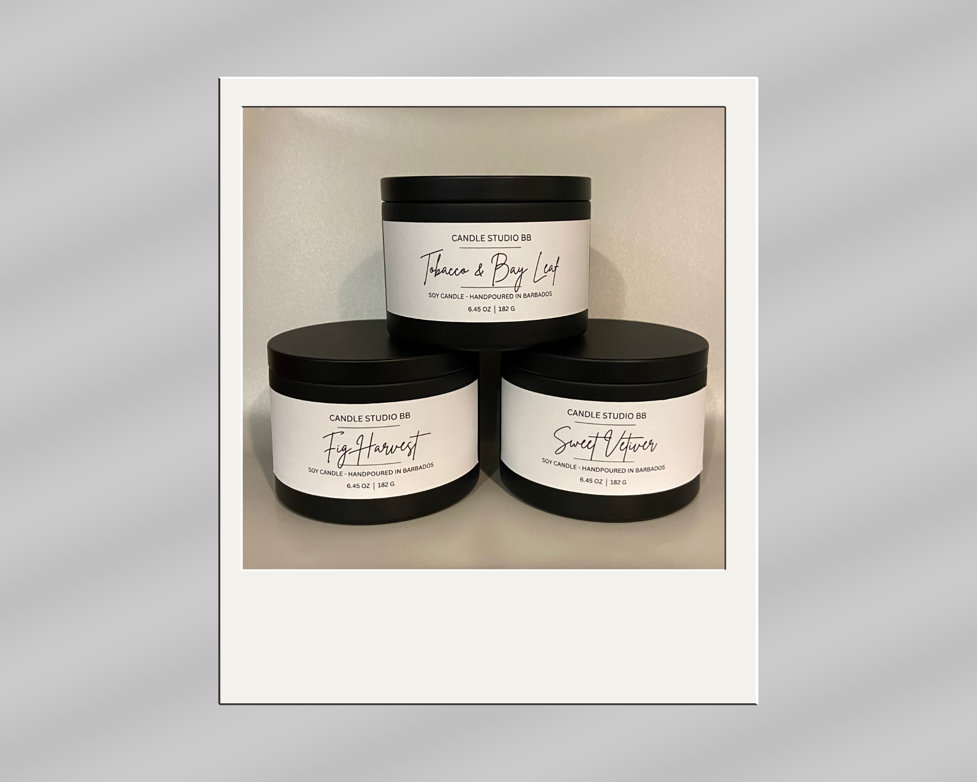 Three black candle jars with white labels displaying different scents: Tobacco & Bay Leaf, Fig Harvest, and Sweet Vetiver, arranged in a pyramid shape against a plain background.