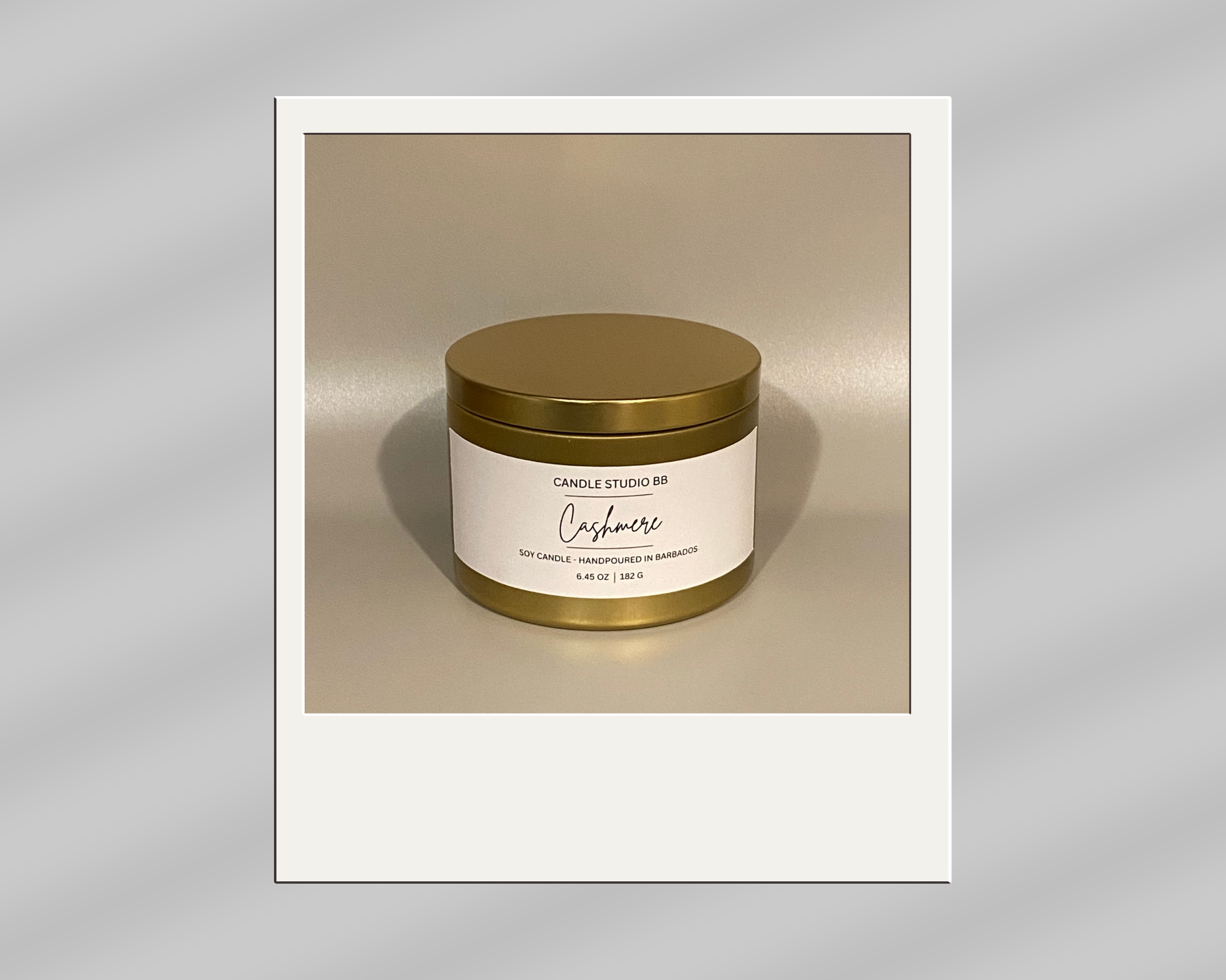 A candle in a gold container with a white label reading "Cashmere" by Candle Studio BB, scented with soy, handcrafted in Barbados, 6.45 oz.