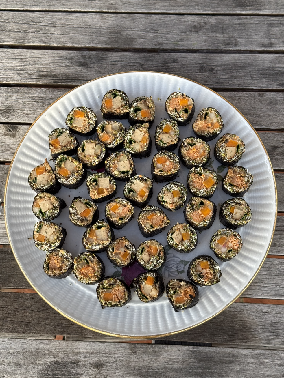 Plate de sushi roulés avec algues, contenant du riz, légumes et poisson, présentée sur une table en bois.