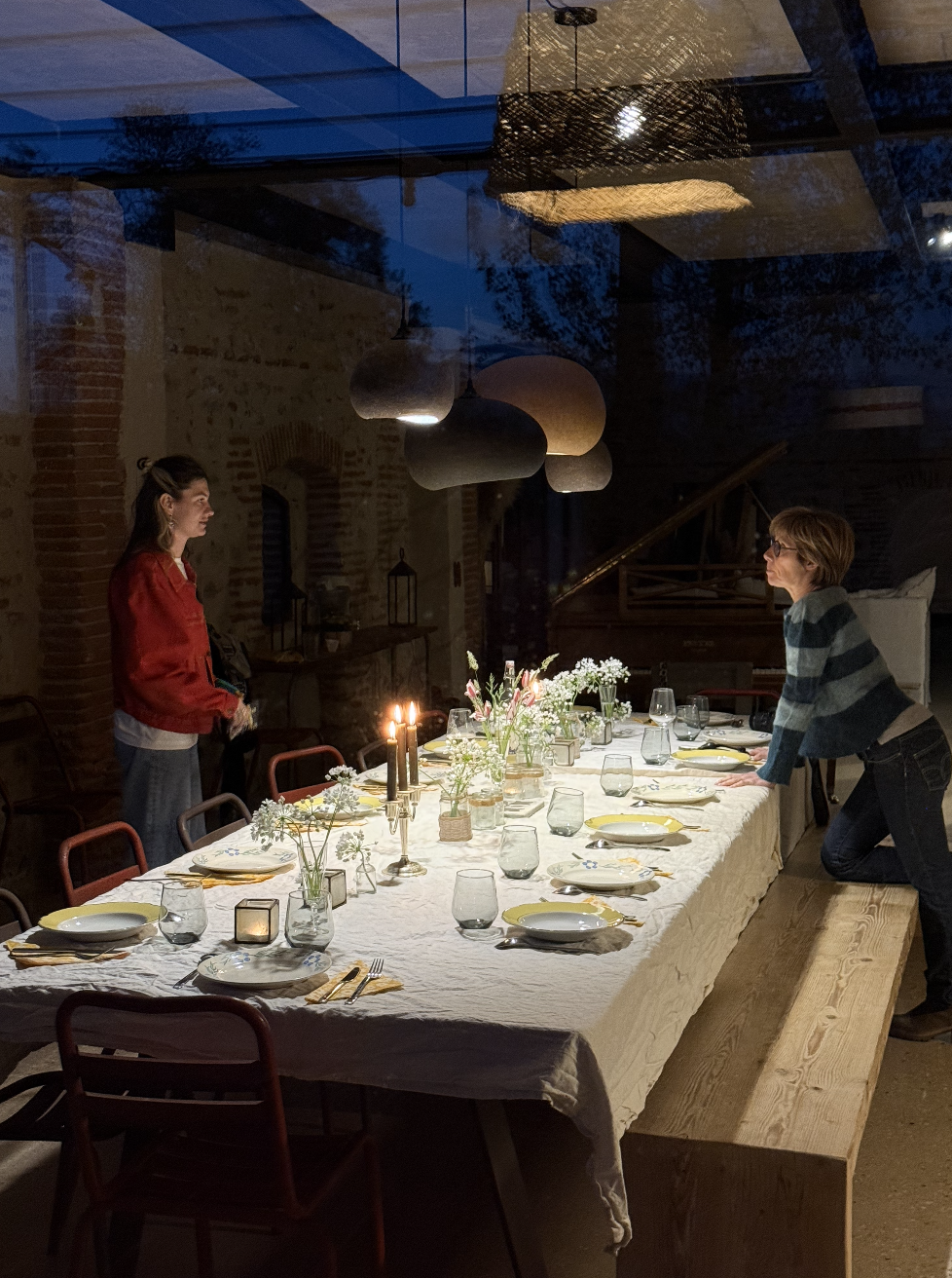 Une table de dîner élégante décorée de vases avec des fleurs, des bougies et des vaisselle, dans un intérieur chaleureux avec deux femmes qui discutent.