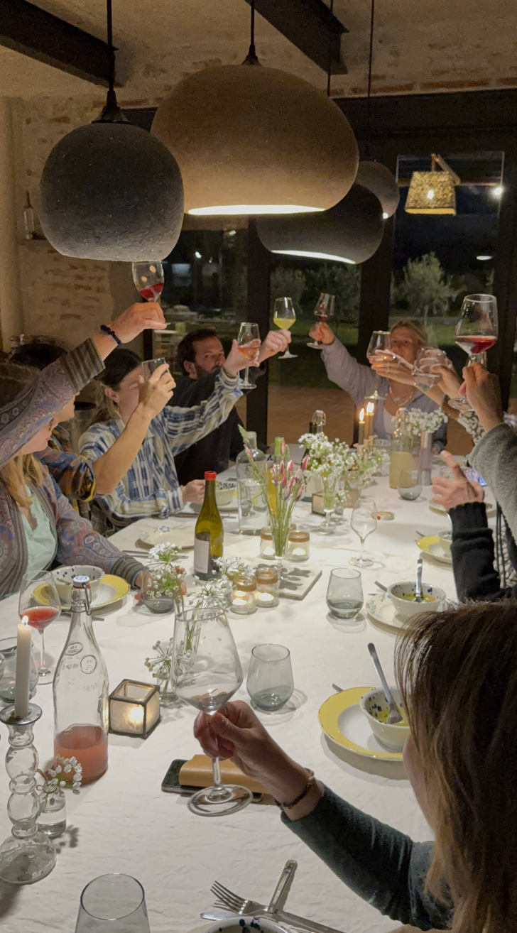 Groupe de personnes à table faisant un toast lors d'une soirée. La table est décorée avec des fleurs, des bougies, des bouteilles et des verres à vin.