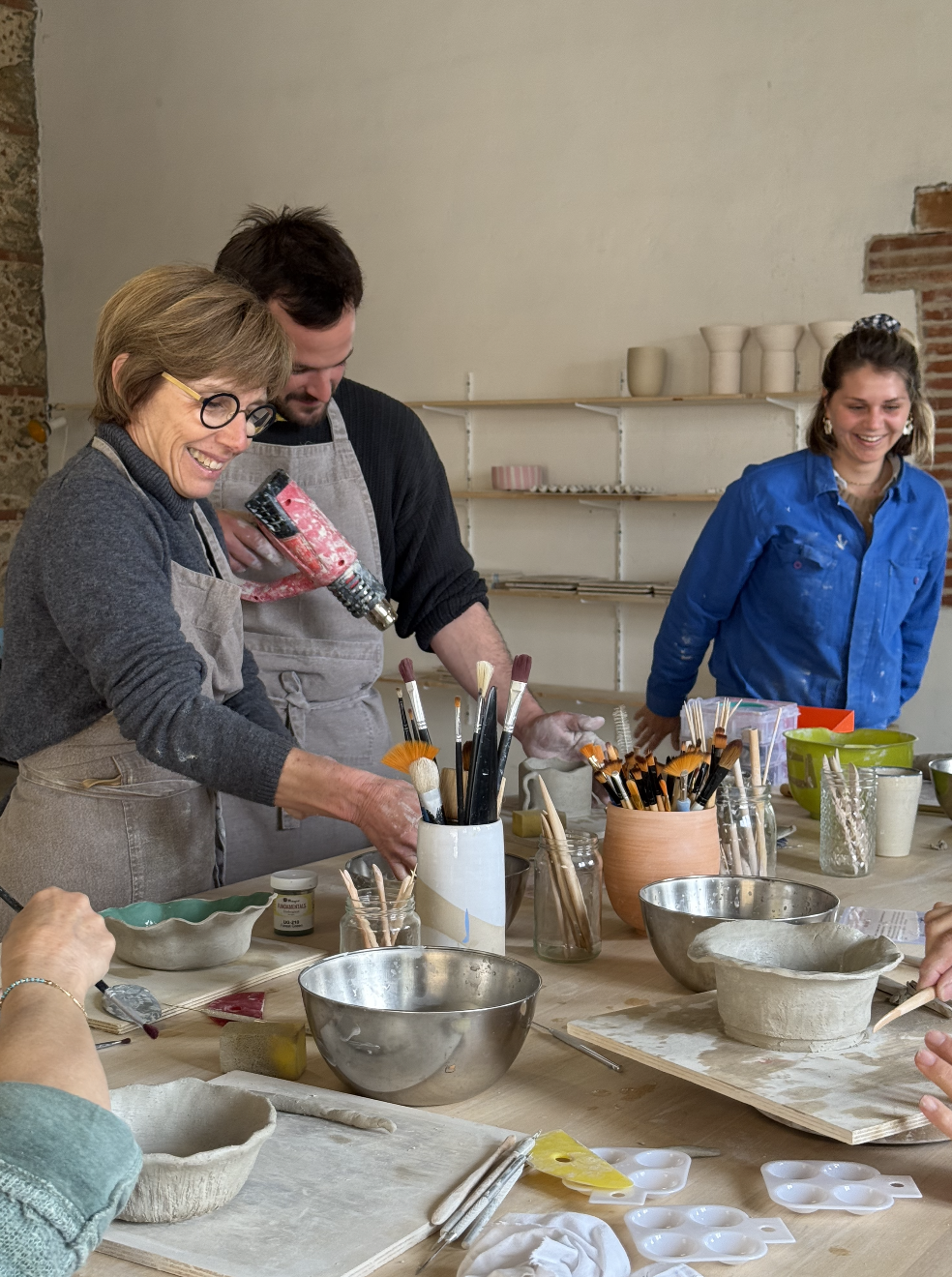 Un groupe de personnes participant à un atelier de poterie, utilisant différentes techniques pour façonner de l'argile, entourés d'outils et de matériaux de sculpture.