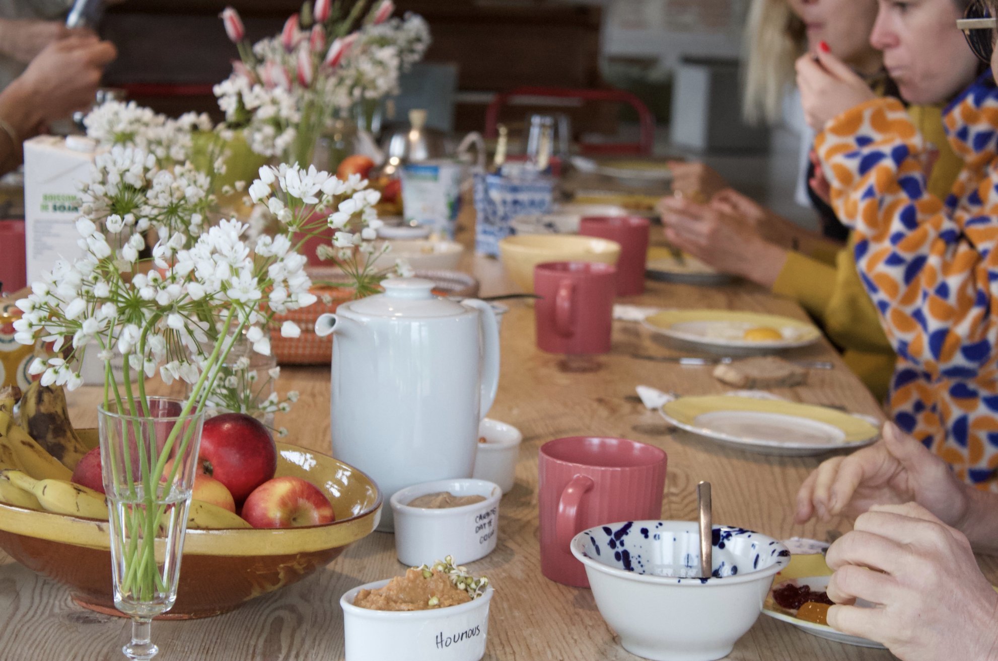 Table à manger avec fleurs, fruits, vaisselle et personnes en arrière-plan