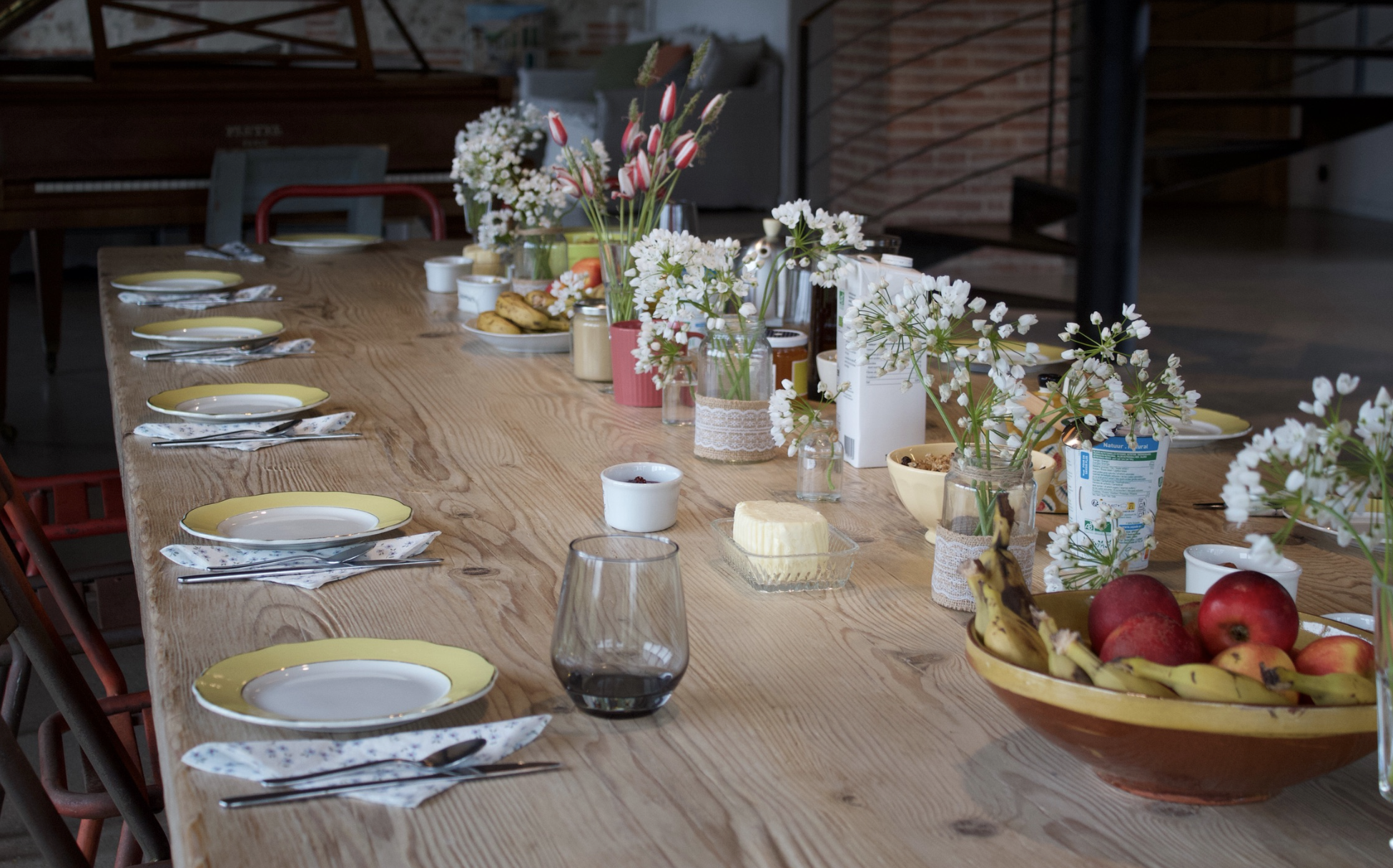 Table en bois long décorée de fleurs, fruits, vaisselle et nourriture pour un repas
