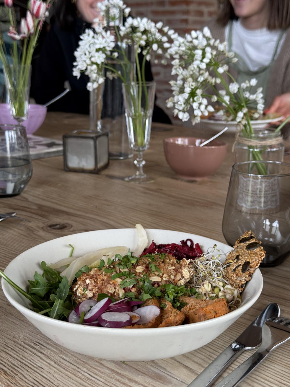 Salade végétarienne dans un bol blanc avec de la verdure, des légumes colorés, des graines, des herbes et un biscuit croustillant, sur une table en bois