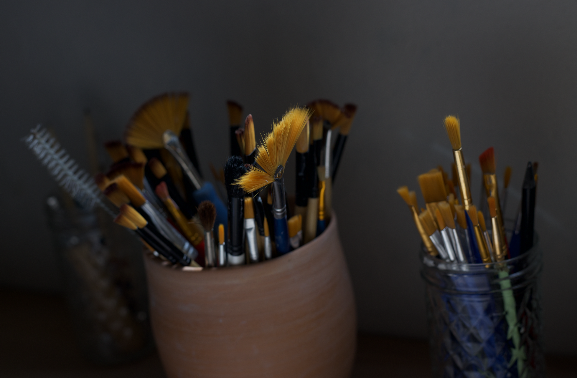 Pots de pinceaux de peinture, avec différents types et tailles, certains avec des poils colorés, sur fond sombre.