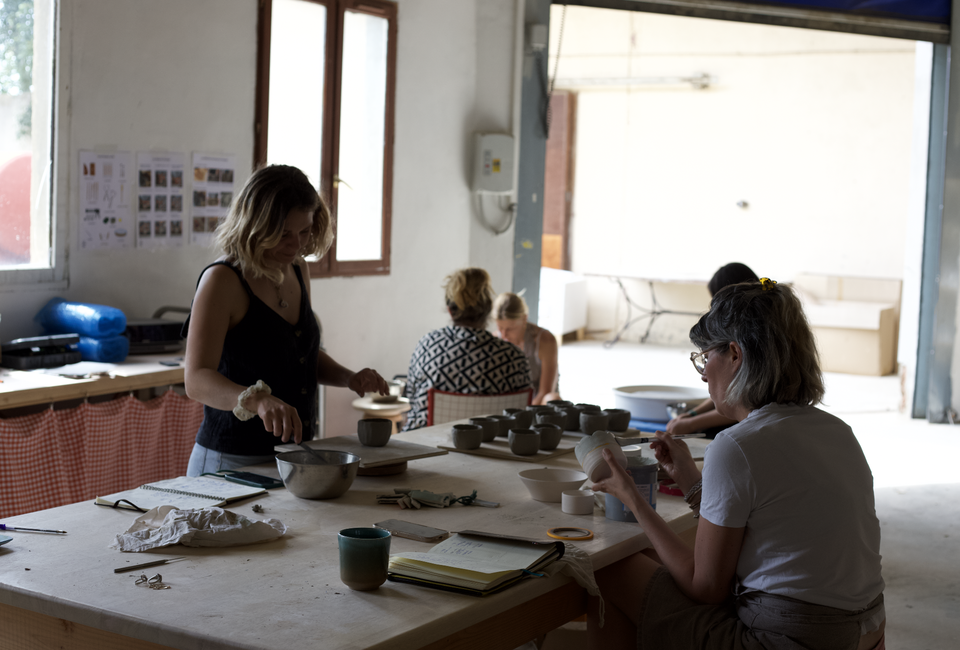 Groupe de personnes travaillant sur de la poterie ou de la céramique dans un atelier avec des outils et des céramiques en cours de fabrication.