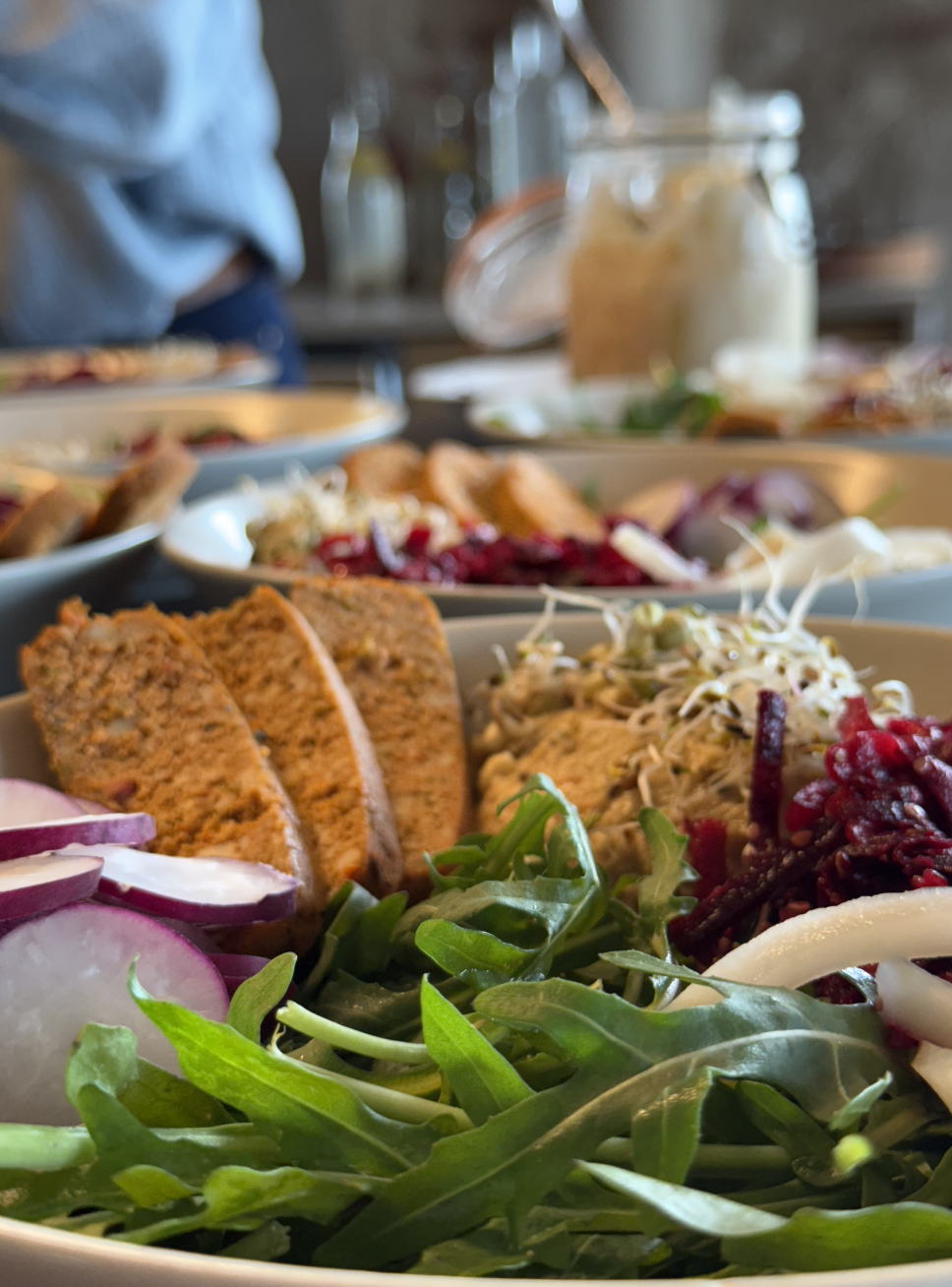 Assortiment de plats de salades avec légumes, légumineuses, et tartes, servis dans une assiette blanche, dans un environnement de restaurant.