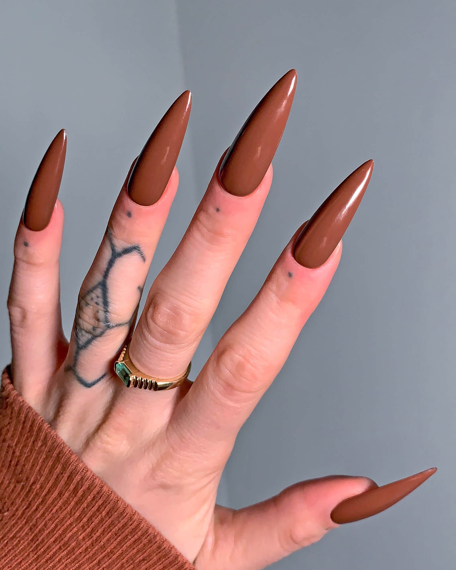 Espresso nail set on a tattooed model standing in front of a grey wall.