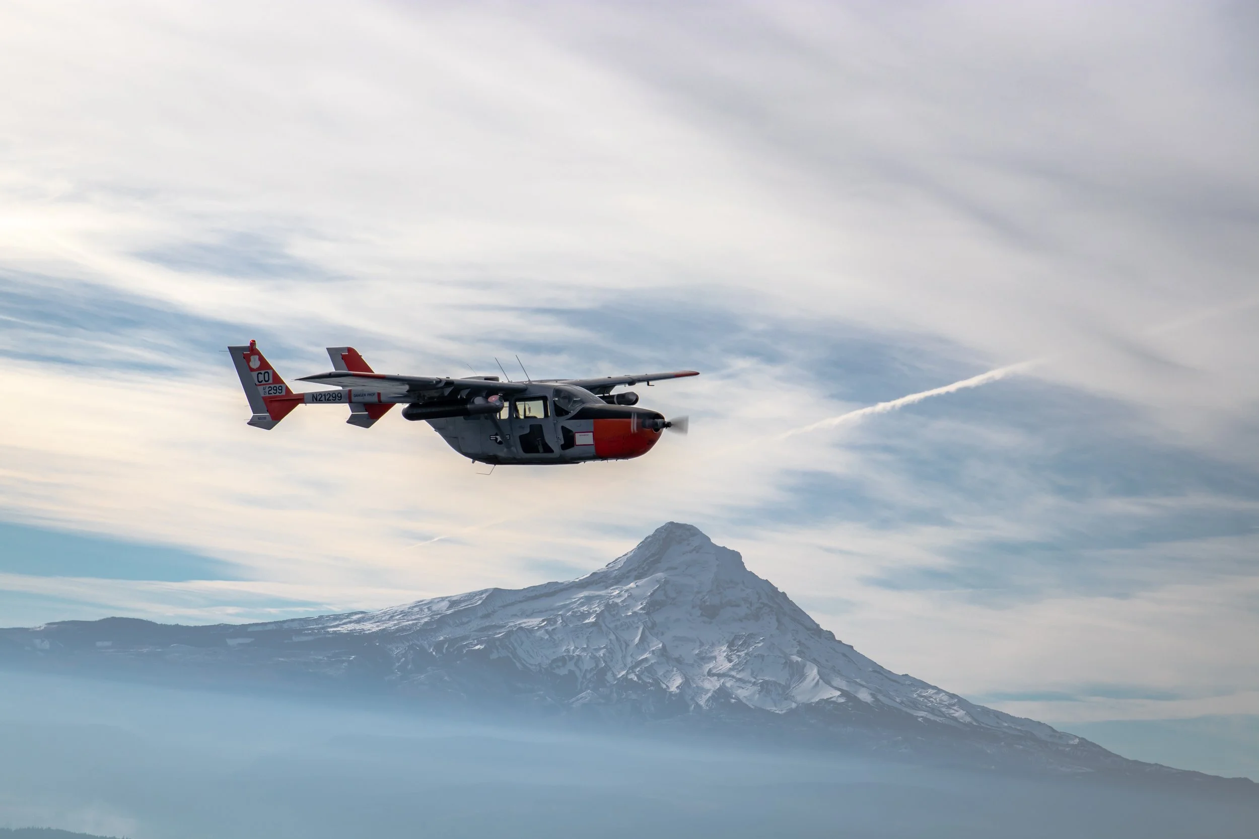 A twin-engine reconnaissance aircraft flying past a snow-covered Mount Hood, Oregon, with a dramatic sky in the background — showcasing aerial capability and mission readiness.