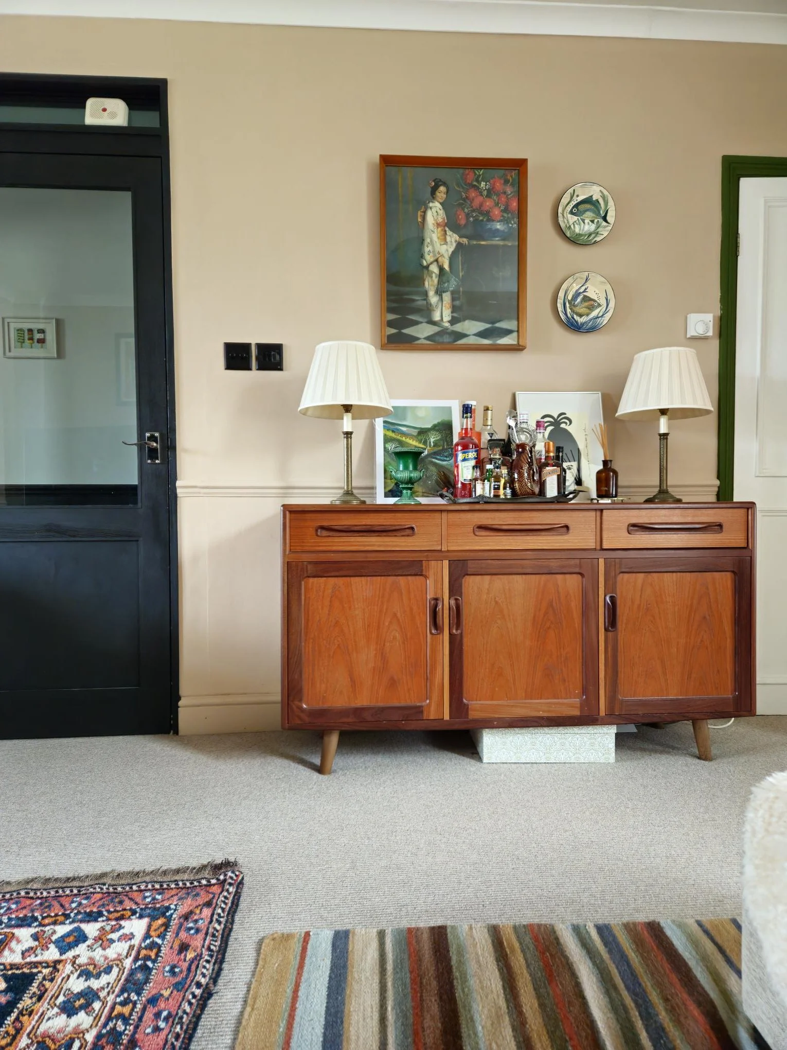 The sideboard in the living room. With a bar tray, lamps for ambiance, and a gallery wall. It's multi-functional, decorative, social and houses cutlery, plates and glasses. Eclectic but intentional.