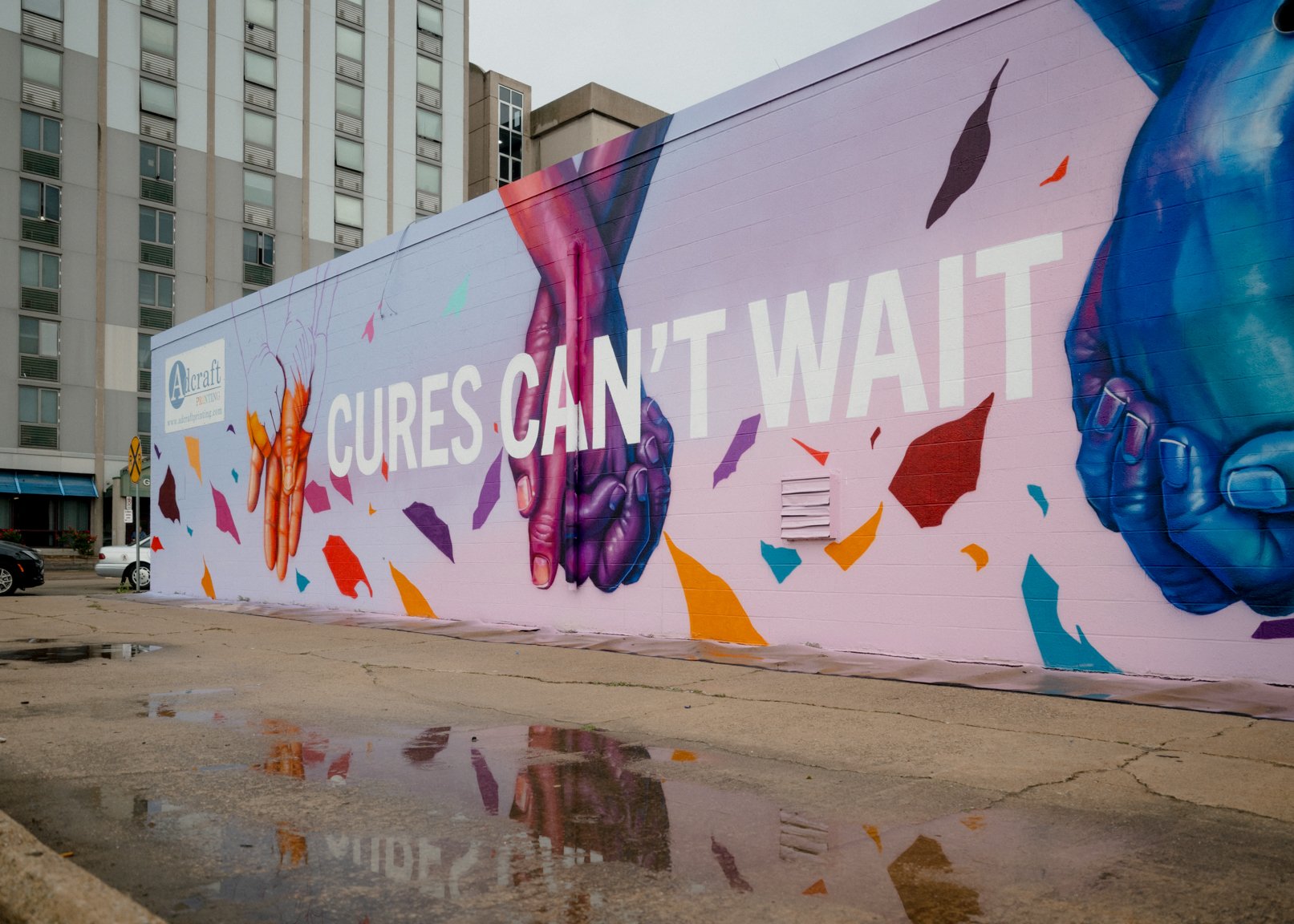 The Cures Can’t Wait mural, with colorful hands and ribbons across the wall.