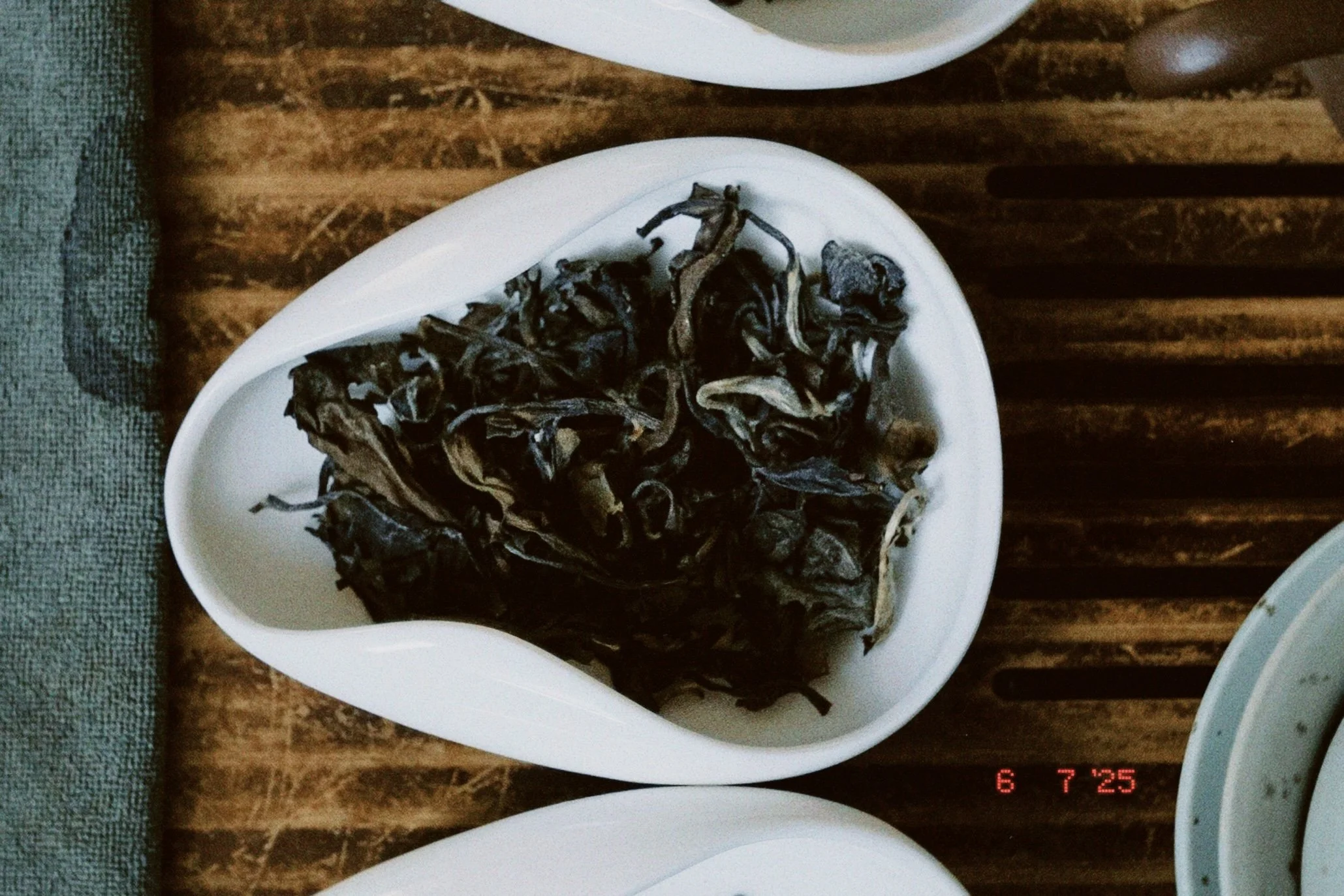 A white, leaf-shaped dish filled with dried, dark-colored mushrooms on a wooden table.
