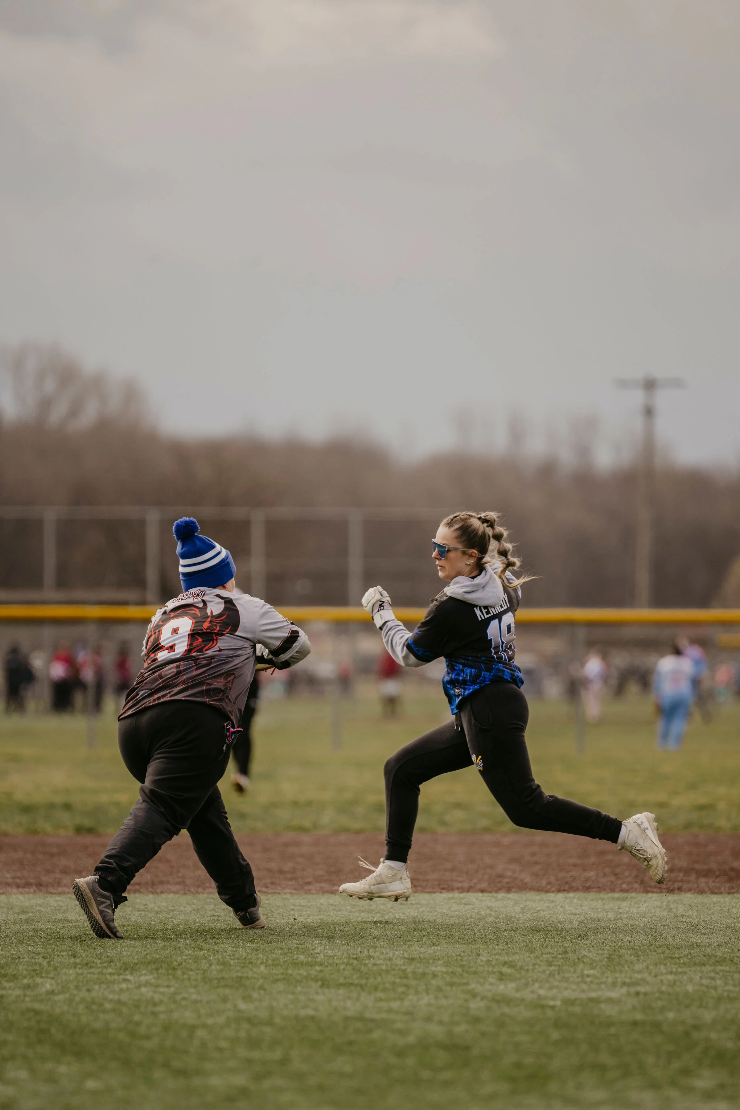 Two people in athletic gear engaged in a friendly sports match on a field, with one person running and the other preparing to catch or block.