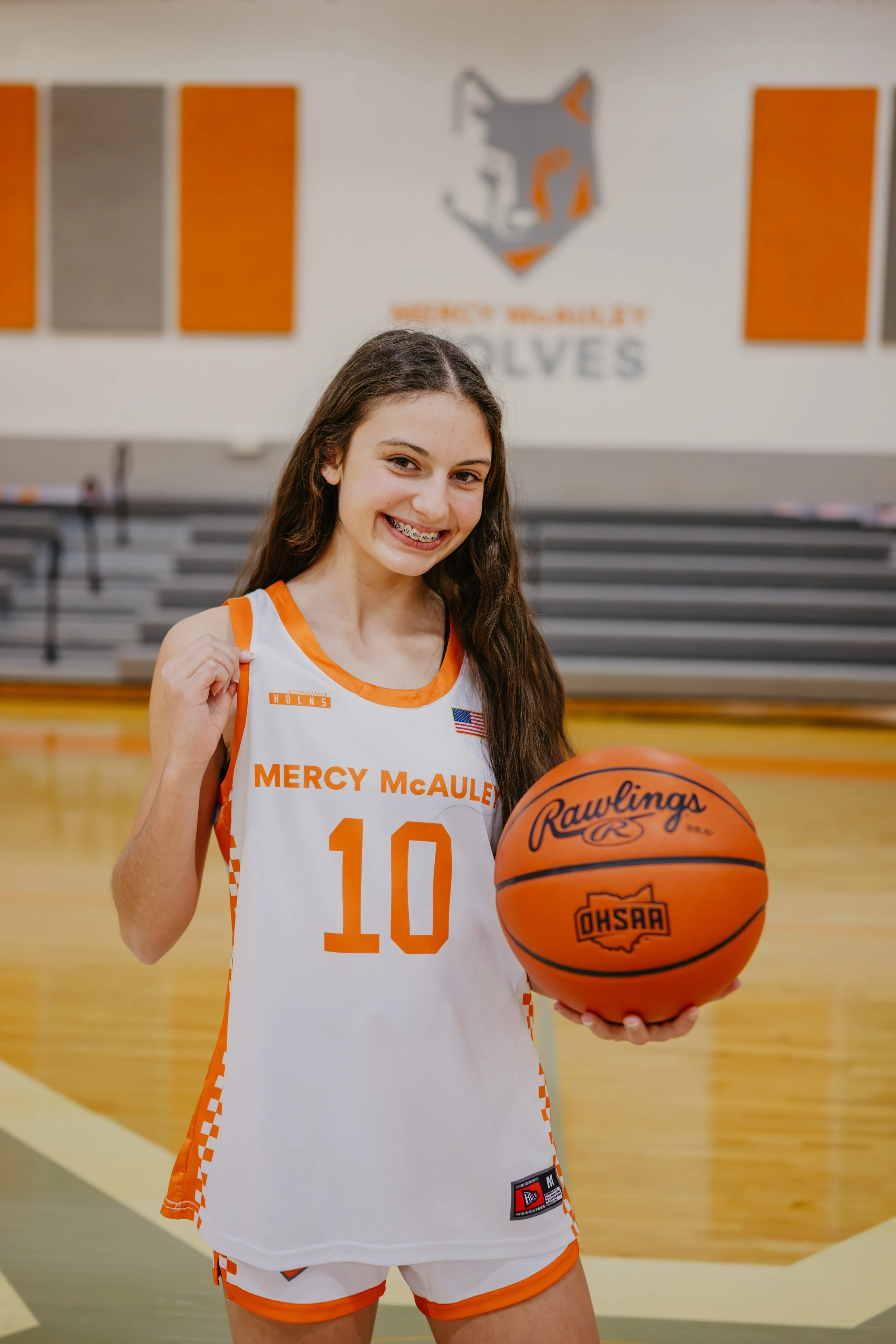 Mercy McAuley Wolves basketball player number 10 pulling jersey and holding Rawlings basketball on gym court