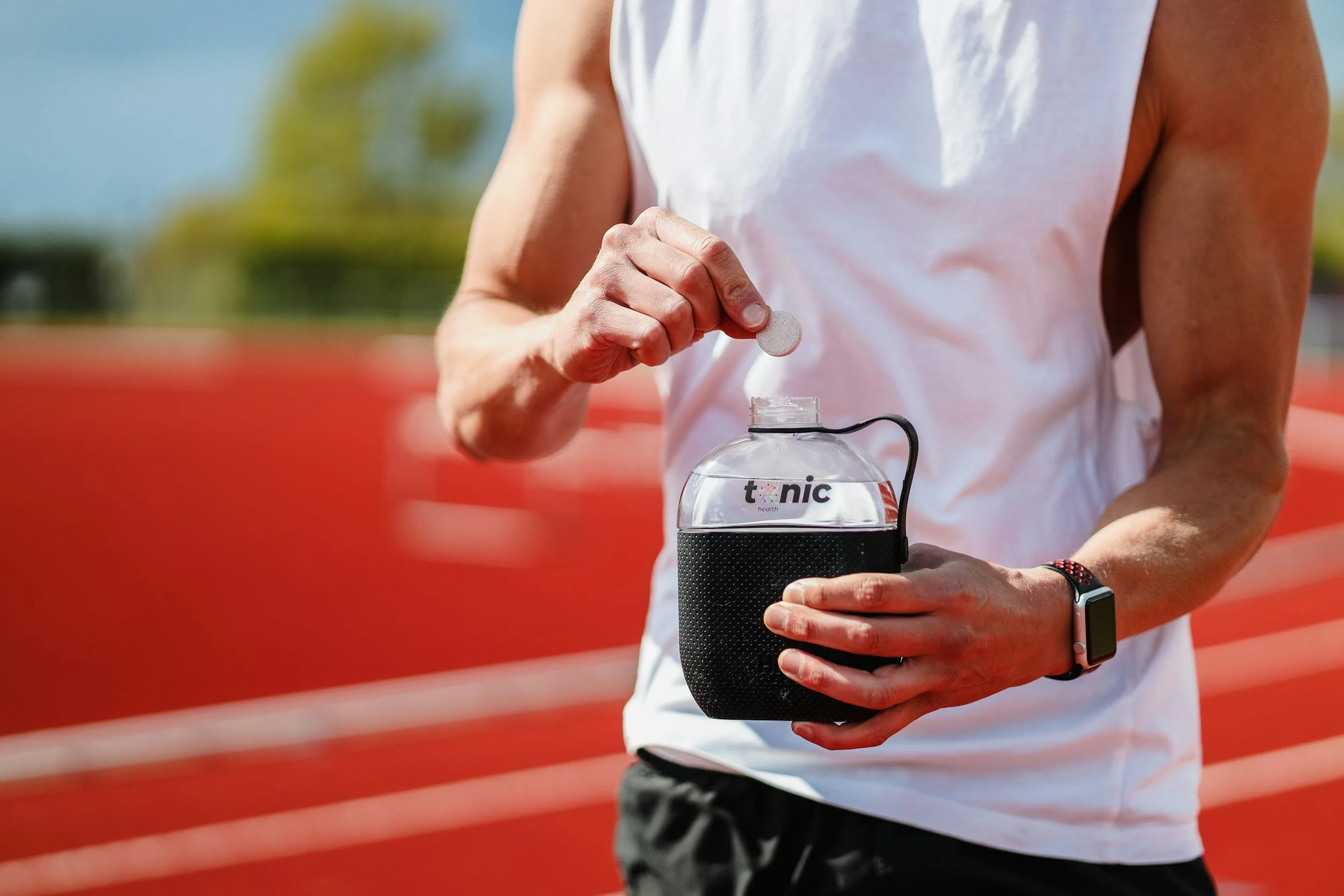 A male runner dropping an electrolyte tablet into a water bottle on a red running track.
