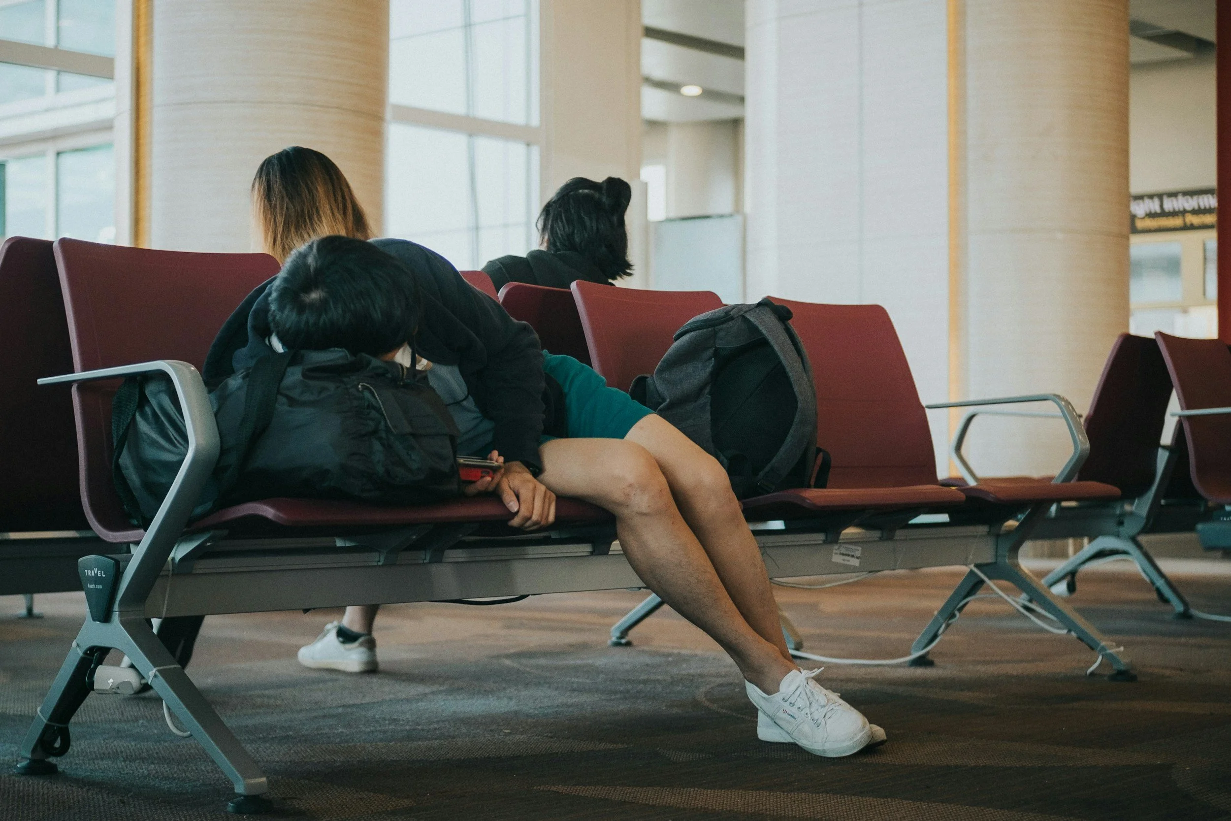 Tired traveler slumped over airport terminal seating with backpacks while waiting for a flight